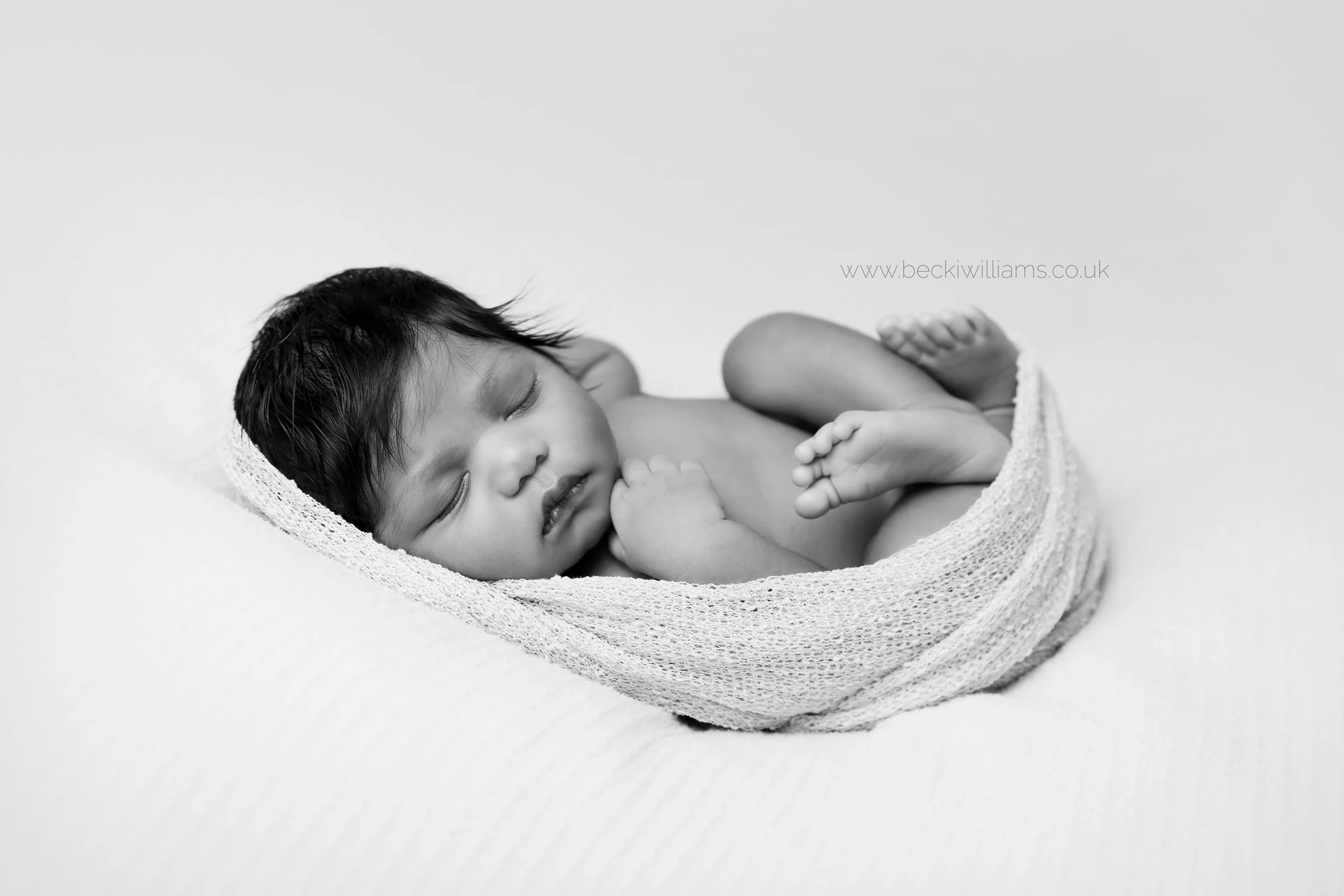 newborn baby girl laying on her back for her newborn photo shoot in hemel hempstead in black and white