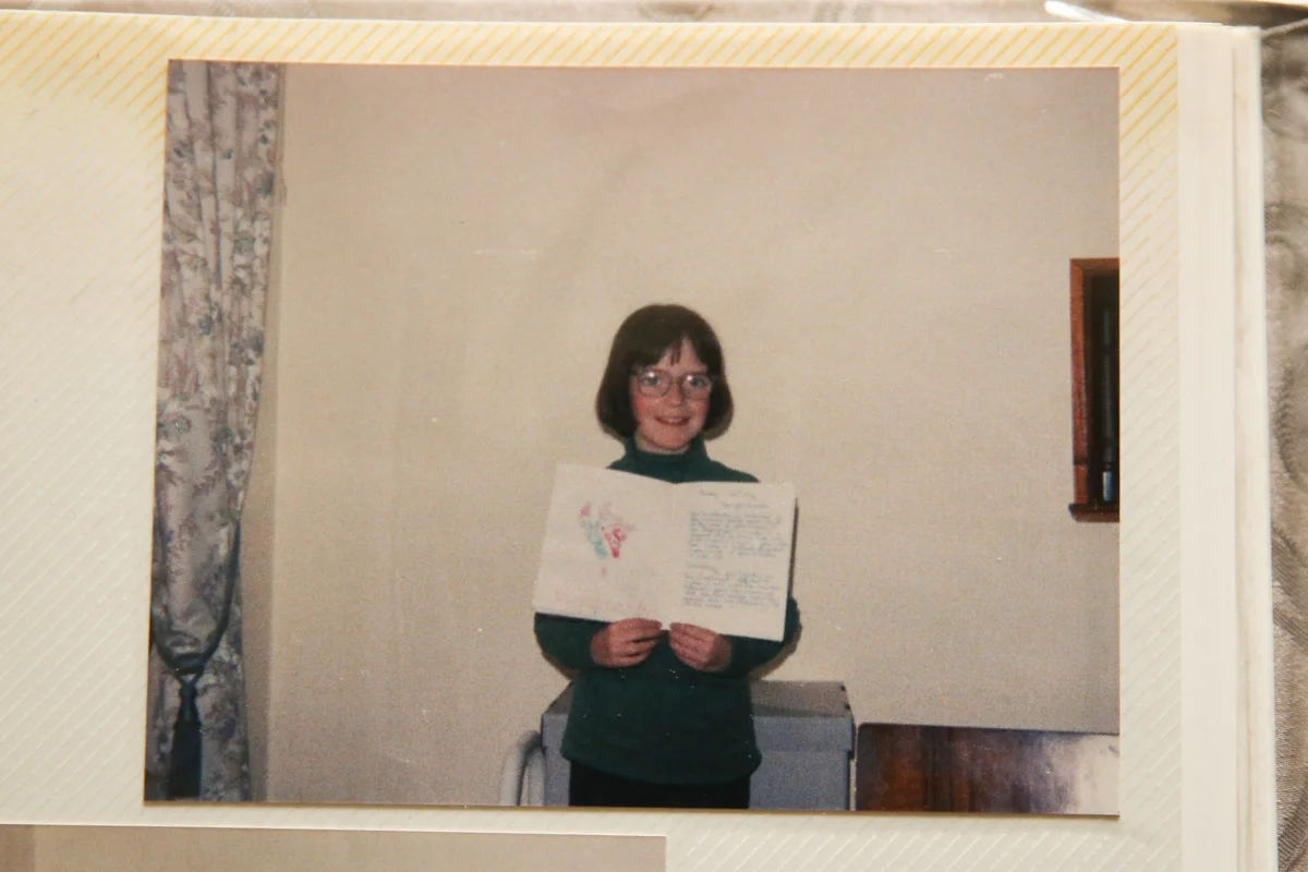 young girl in the early 90s holding a school book proudly