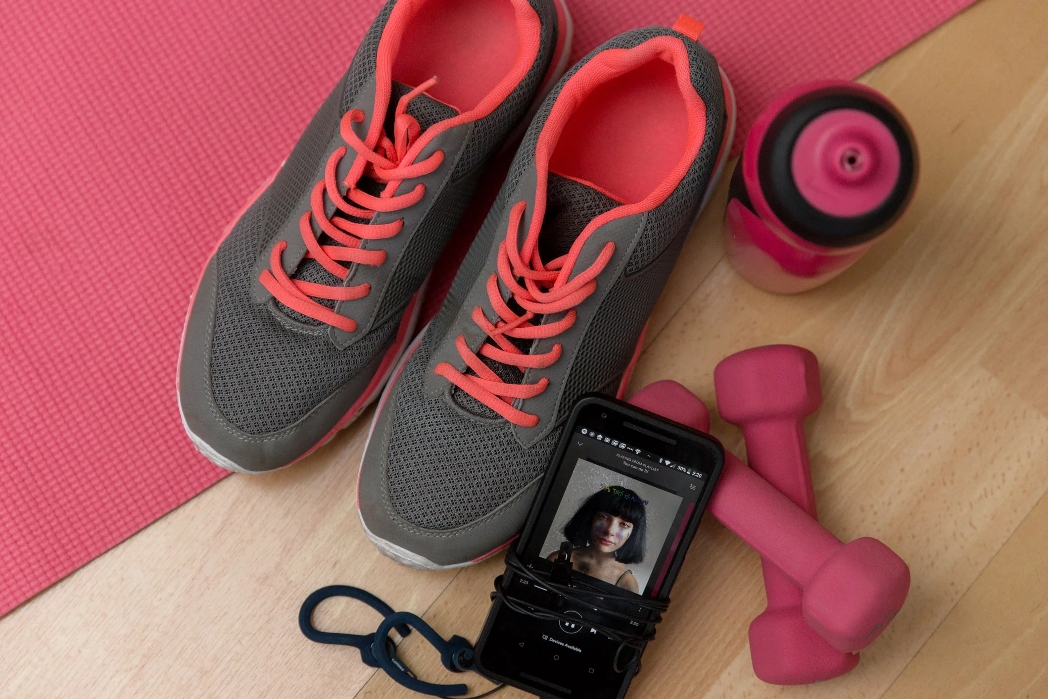 trainers, weights, water bottle and a phone on a pink gym map and wooden floor