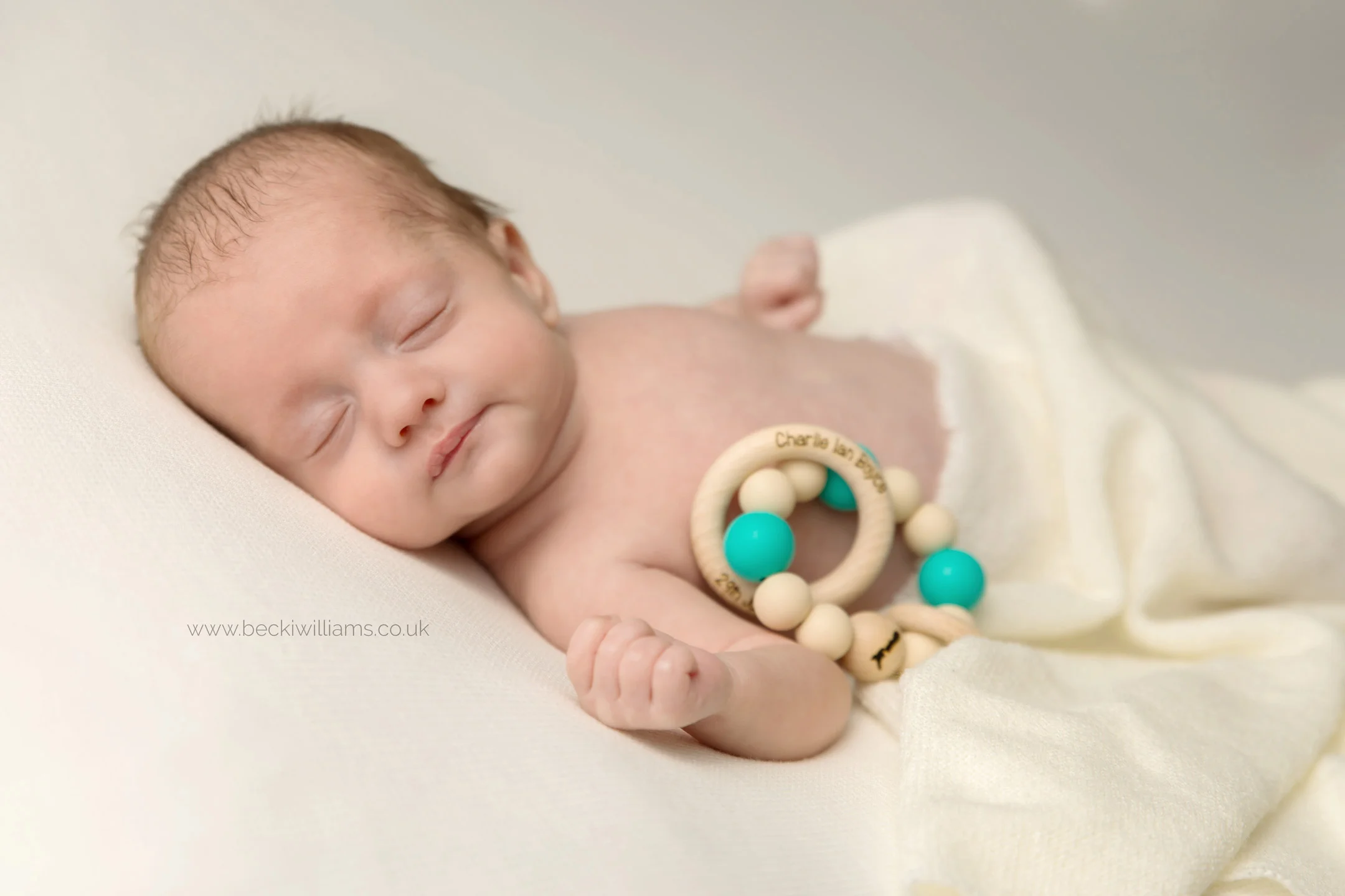 newborn baby boy lays sleeping with his teether, covered in a cream blanket