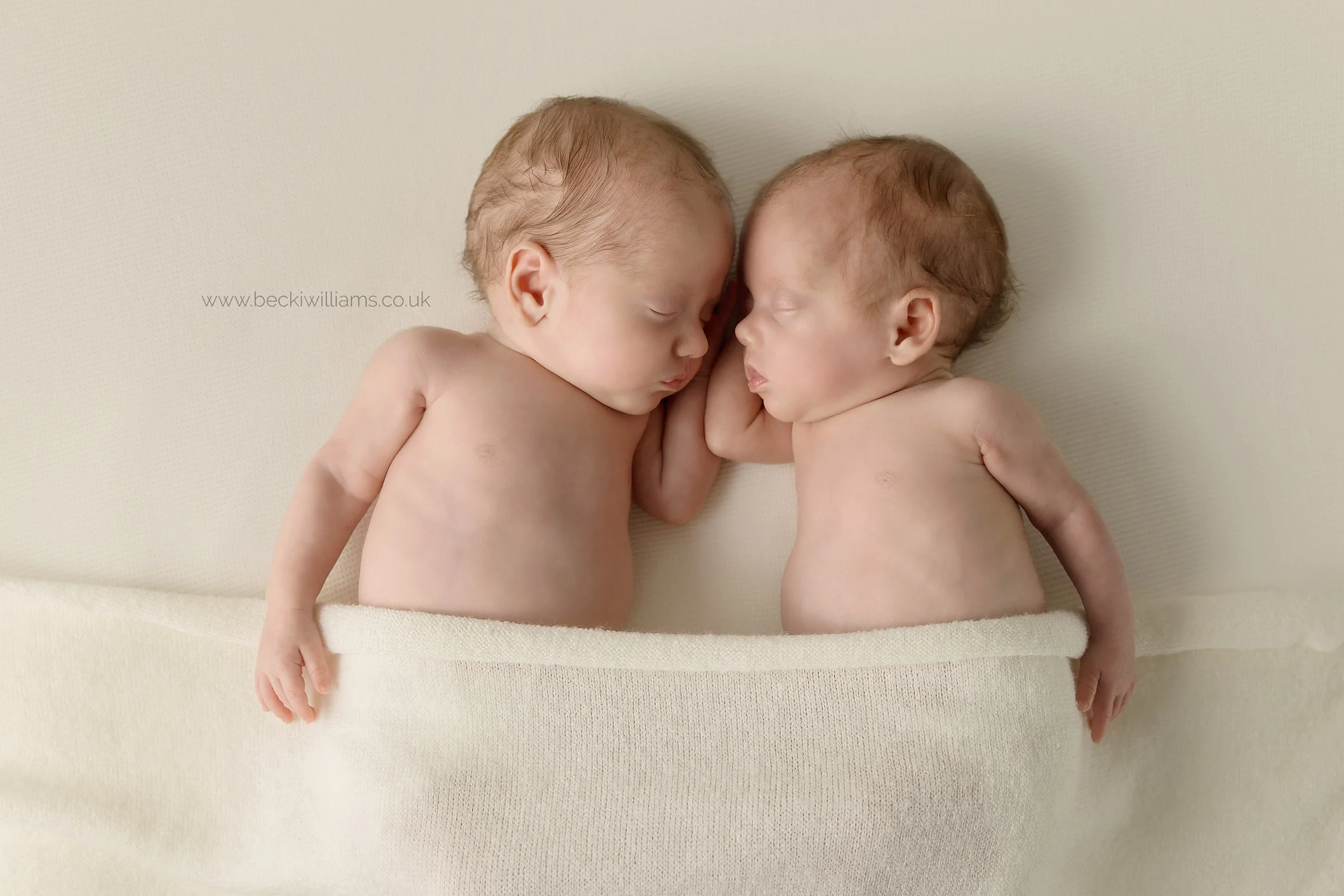 newborn twins sleep next to each other covered in a cream blanket for their newborn photography shoot in hemel hempstead