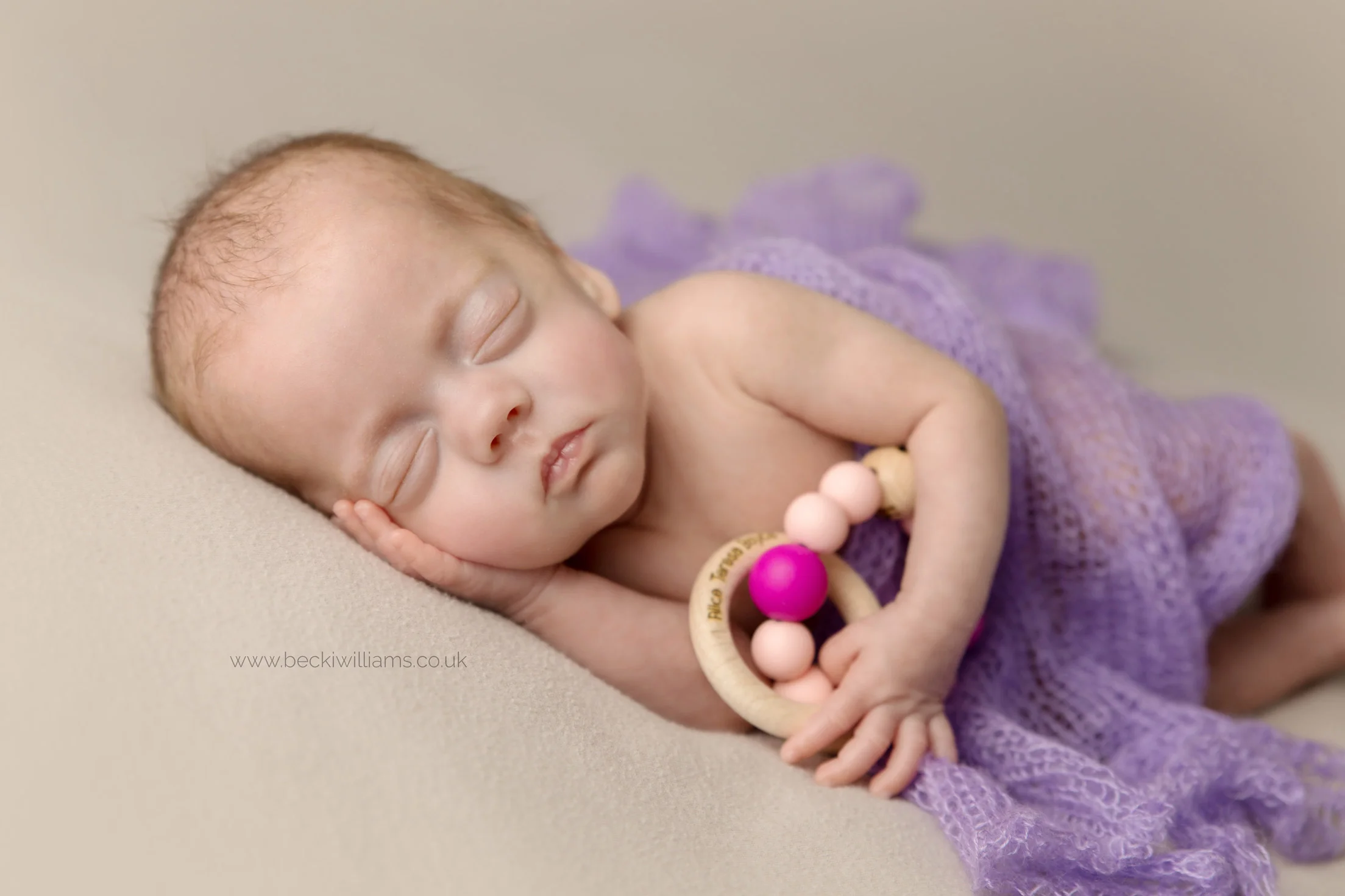 newborn baby girl lays asleep holding a wooden theether.