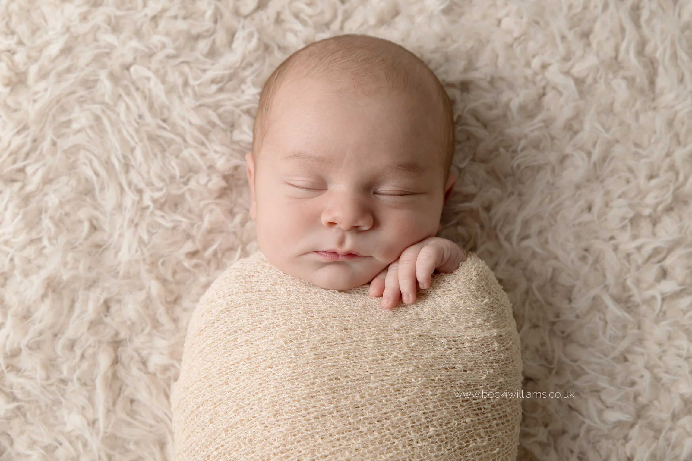 sleeping newborn baby boy wrapped in a cream blanket on a cream fluffy throw