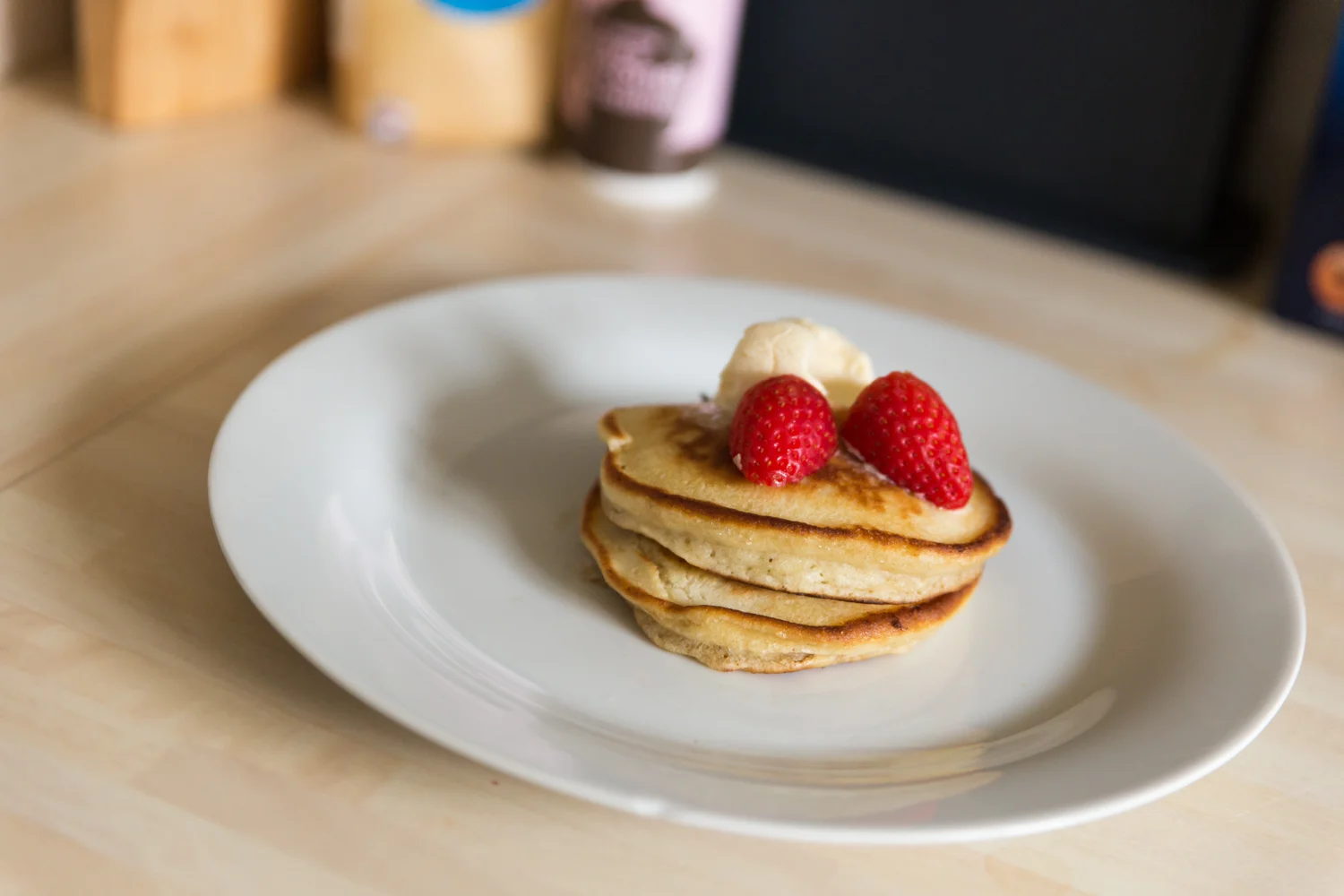 Three american style pancakes on a white plate with ice cream and strawberries on top.
