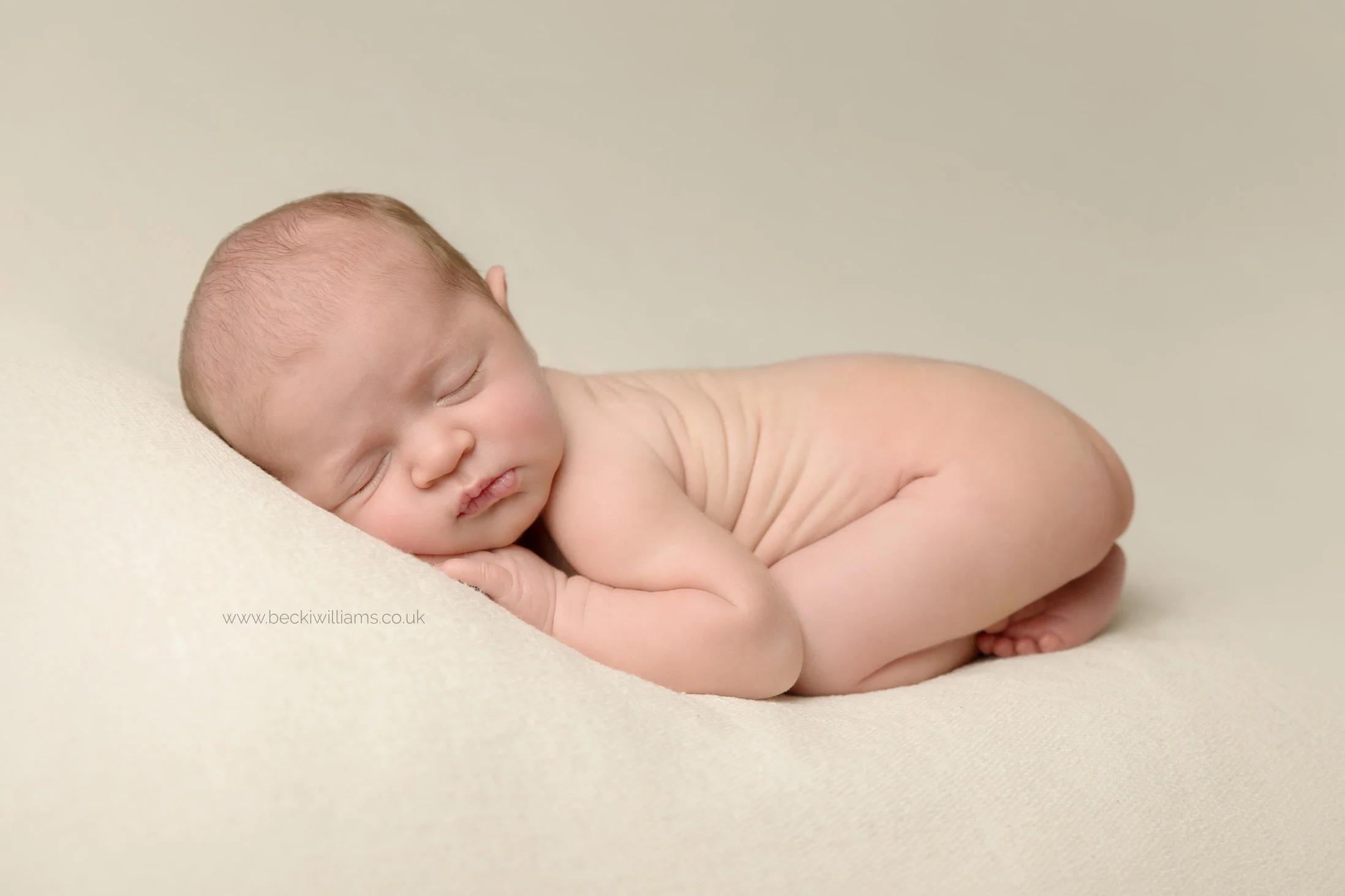 newborn girl laying on her tummy on a cream blanket for her newborn photo shoot