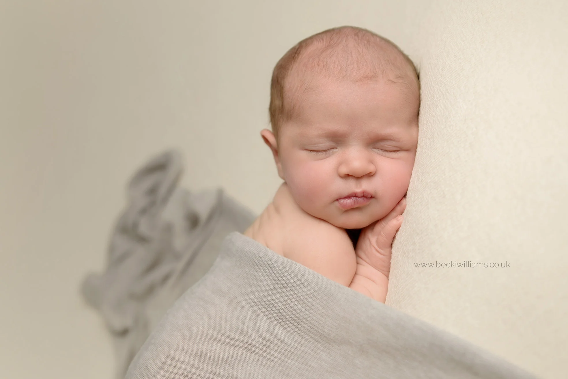newborn baby girl laying on her tummy, covered by a grey blanket at her newborn photo shoot