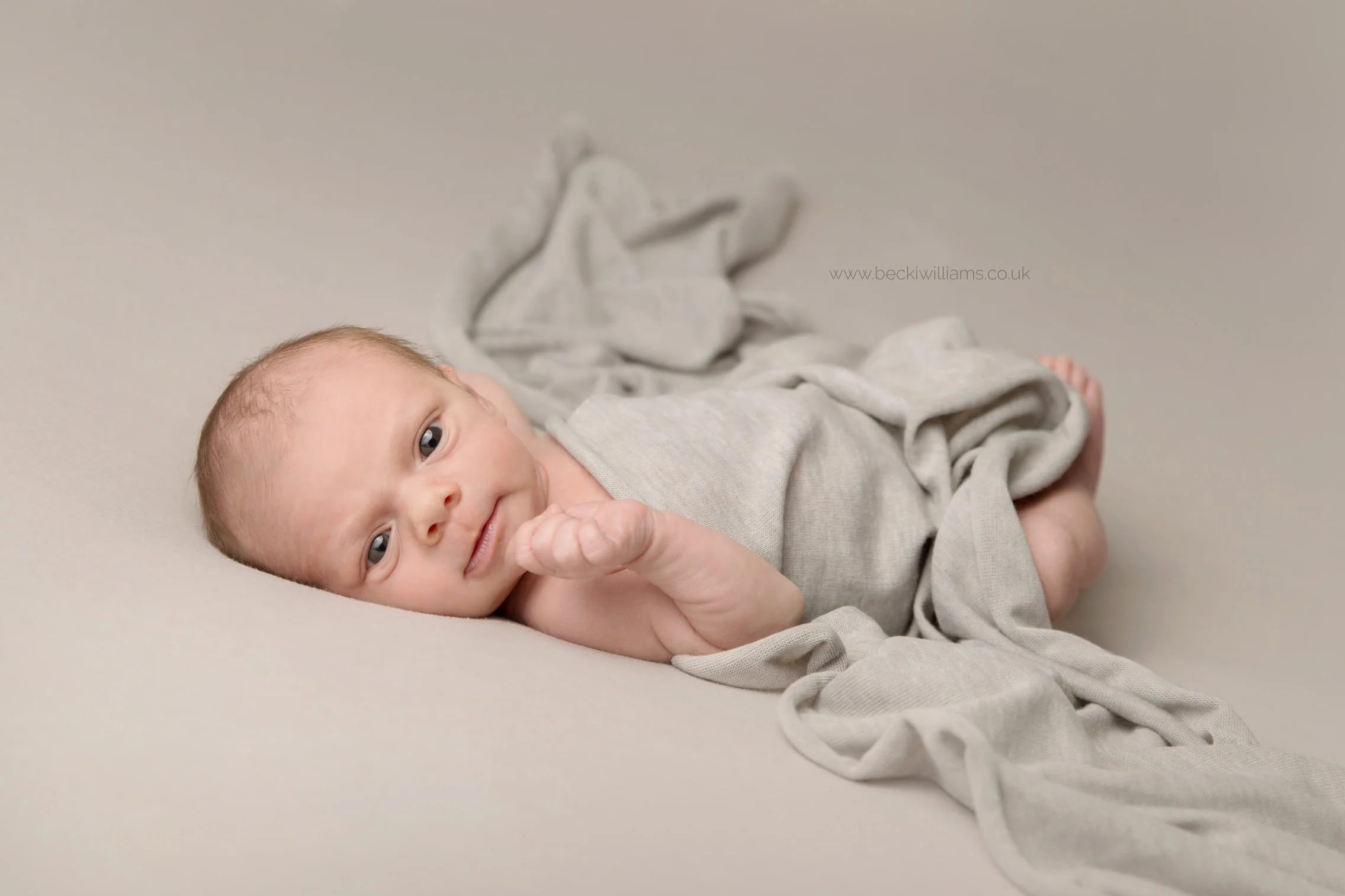 newborn baby lays awake on his back covered in a grey blanket