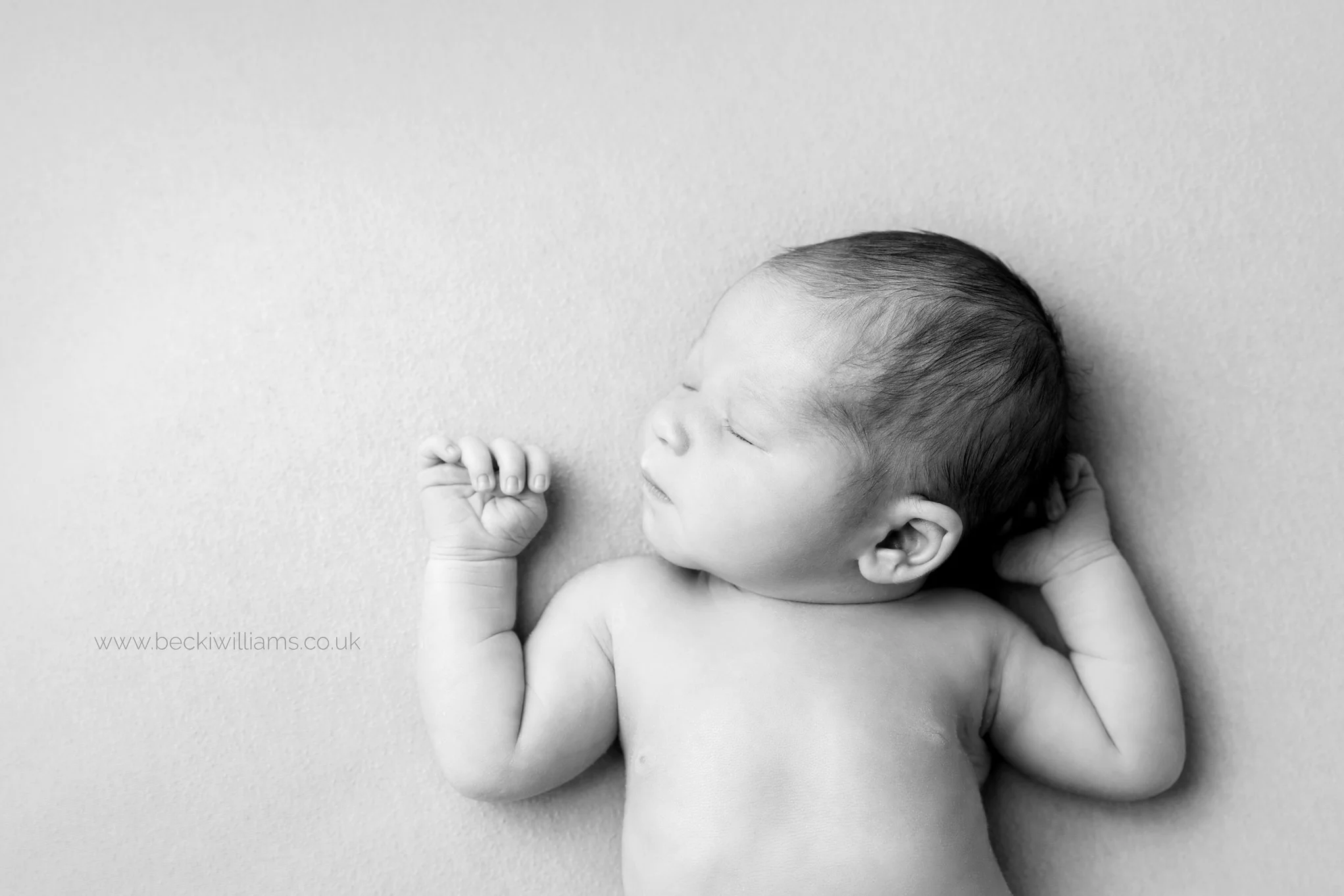 black and white photo of newborn baby laying on his back with his arms by his face