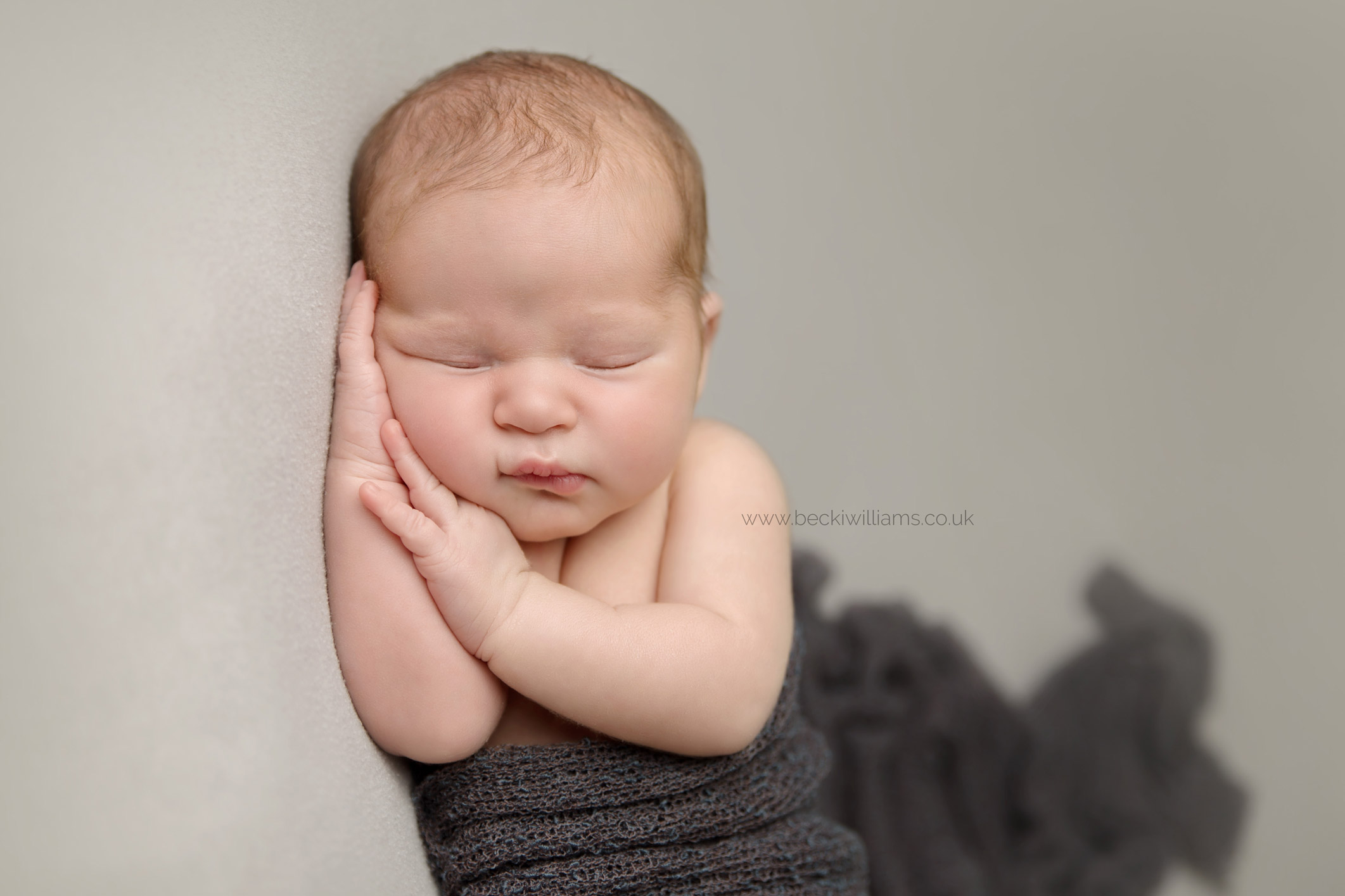 Newborn boy laying on his side covered by a dark grey blanket