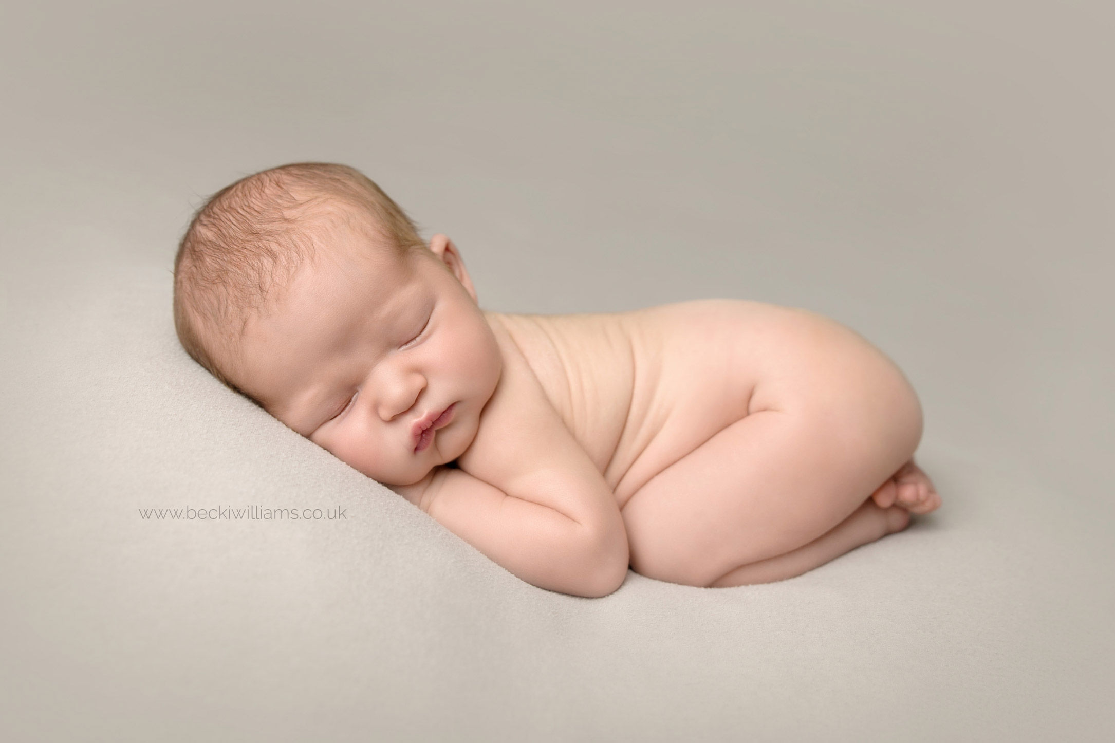 Newborn boy laying sleeping on his tummy on a light grey blanket