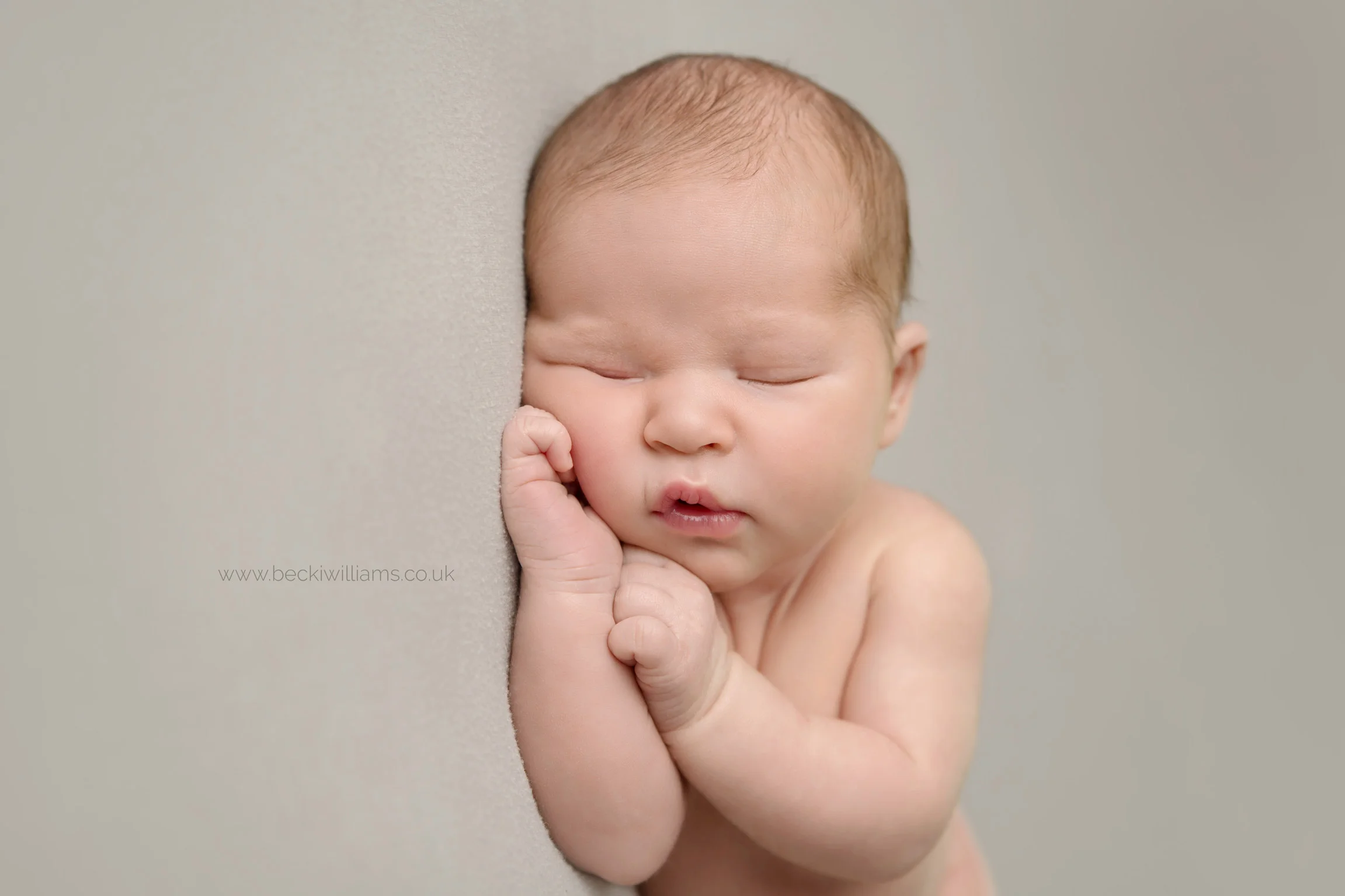 photo of newborn baby boy laying on his side, his cheeked squashed slightly by his hand.