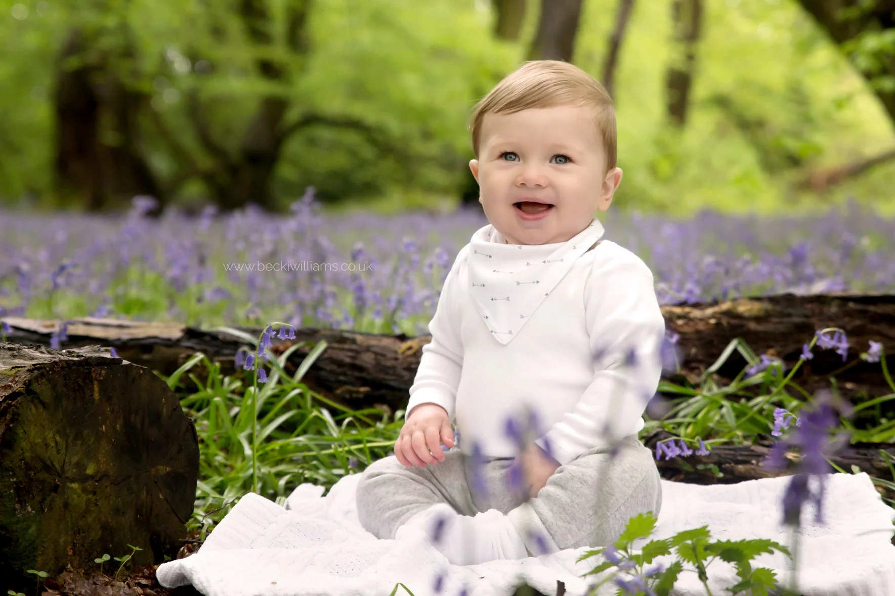 little boy sitting, smiling amongst the bluebells in st albans