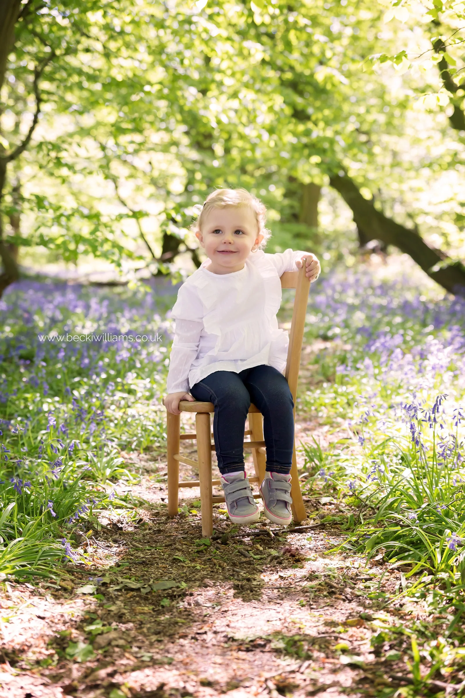 little girl sitting on a chair amongst the bluebells