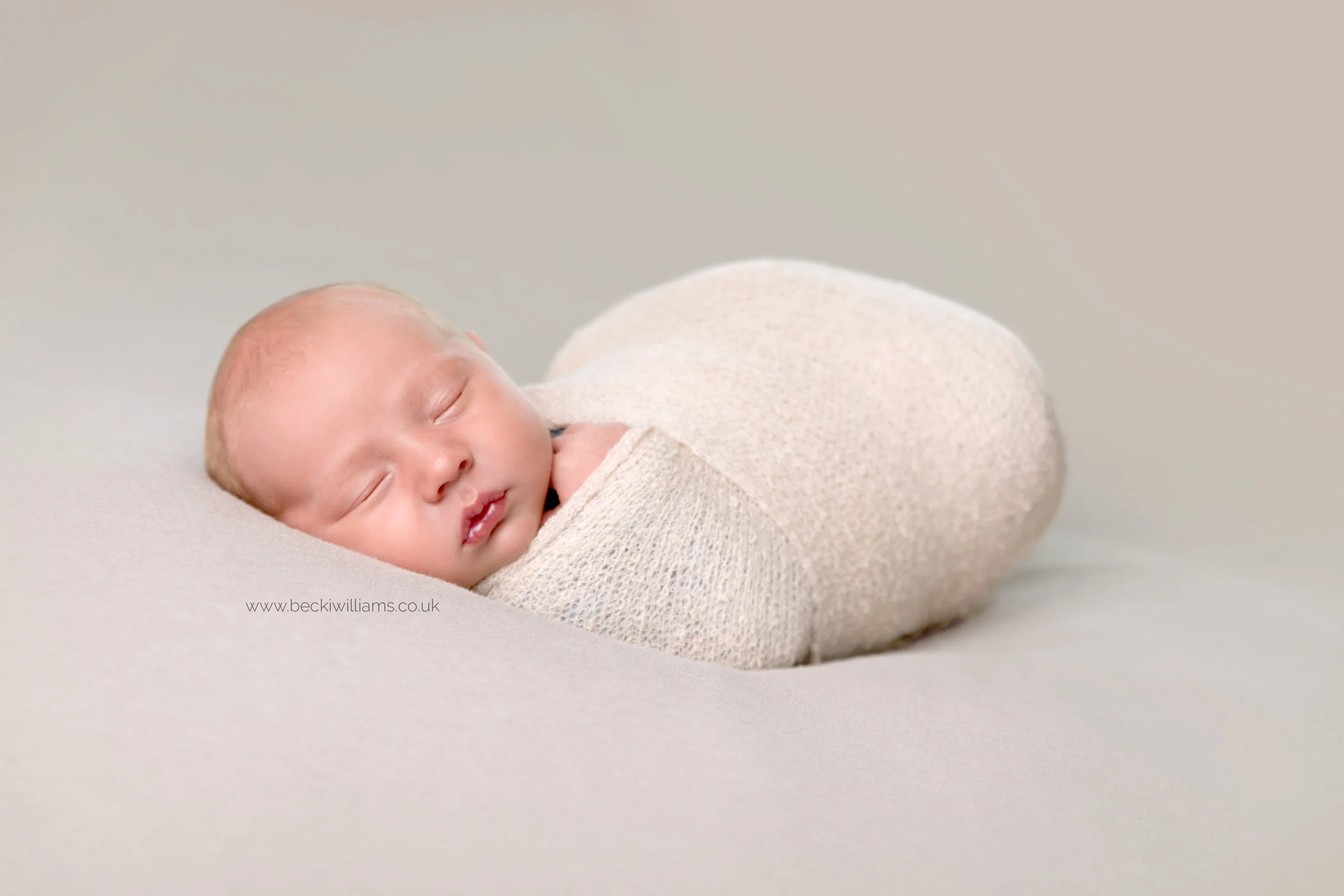 wrapped newborn baby on a grey blanket for his newborn photo shoot in berkhamsted