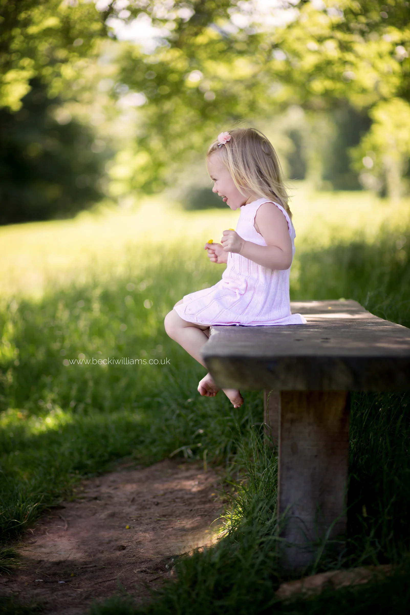 little girl sitting, smiling on a bench in gadebridge park, hemel hempstead