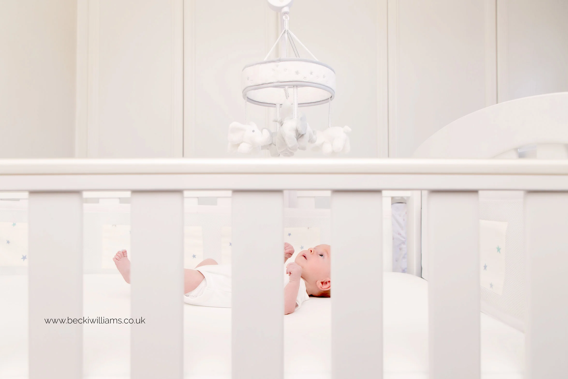 newborn baby girl laying in her white cot for her lifestyle newborn photo shoot in st albans