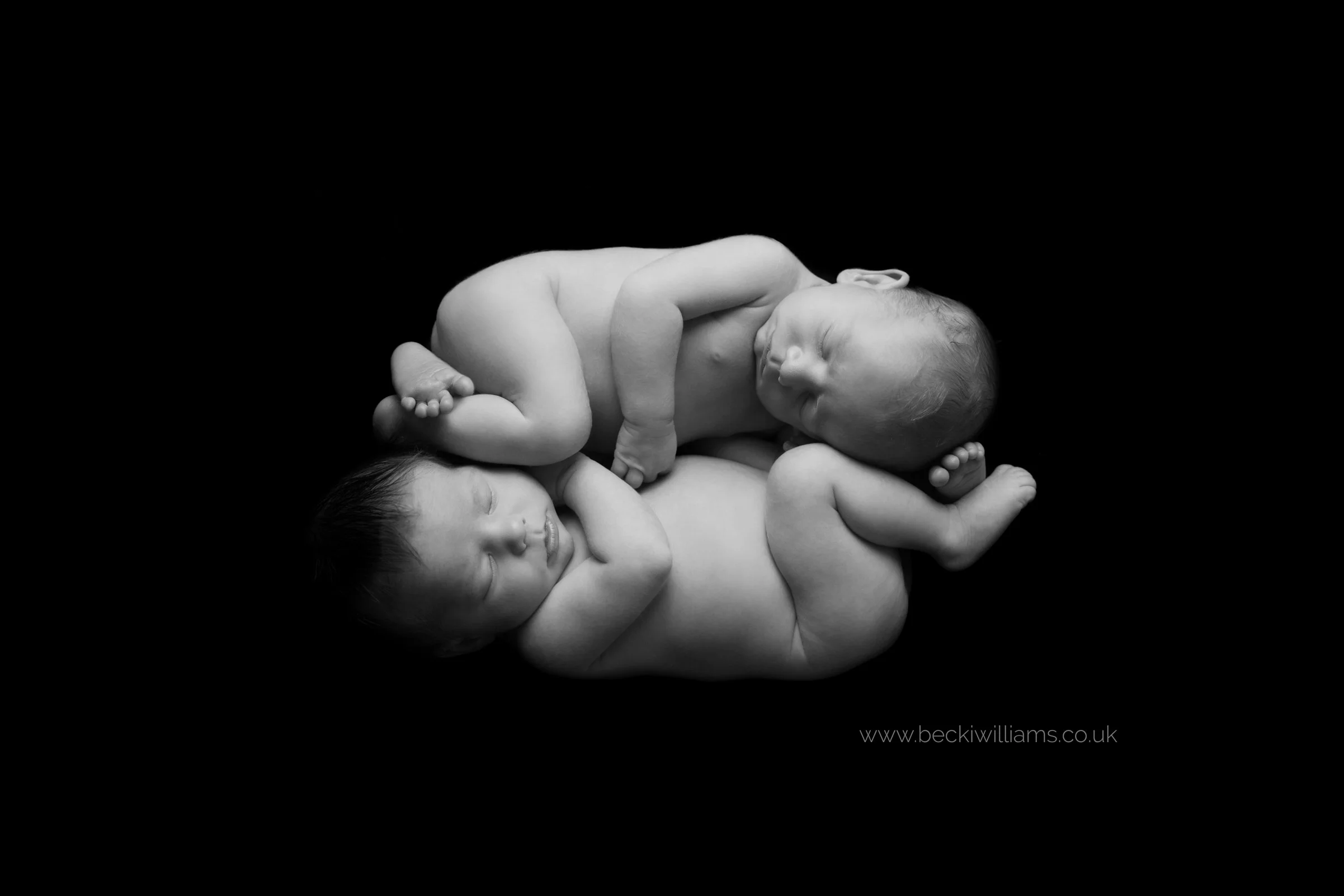 black and white photo of newborn twins laying head to toe, cuddled up to each other at their newborn photo shoot in Hemel hempstead