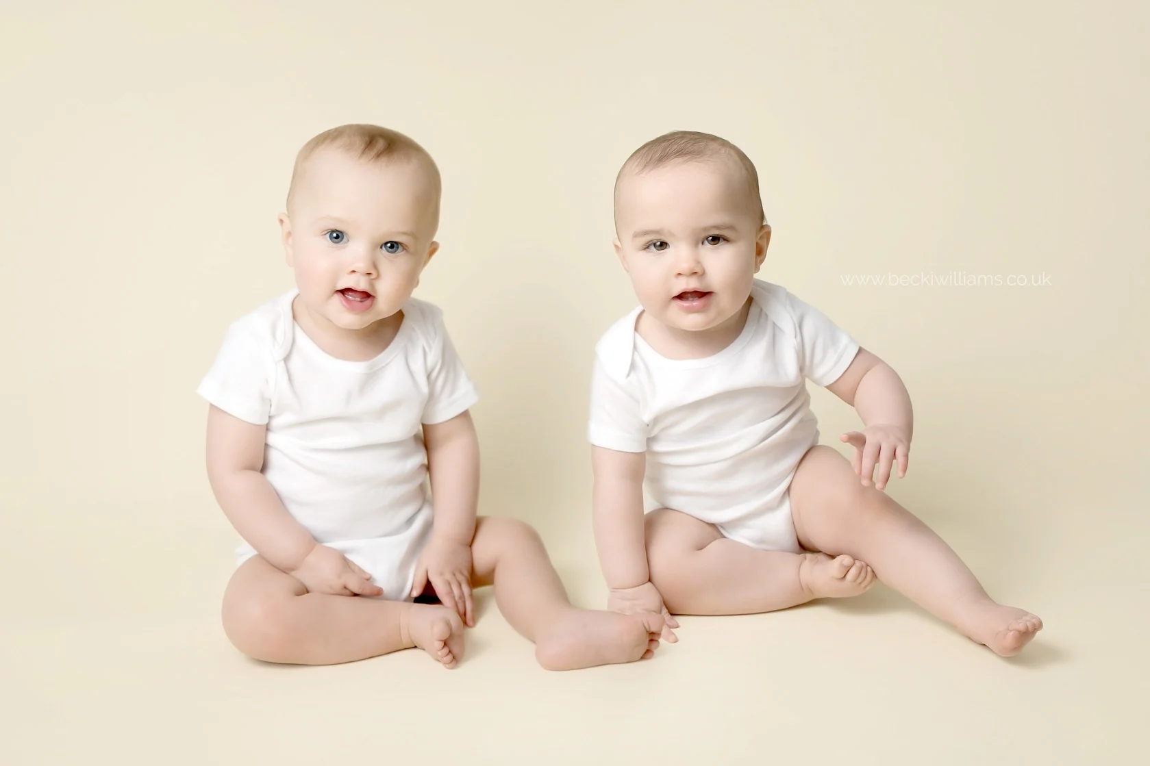8 month old twins in white vests on a cream blanket at their photo shoot in hemel hempstead