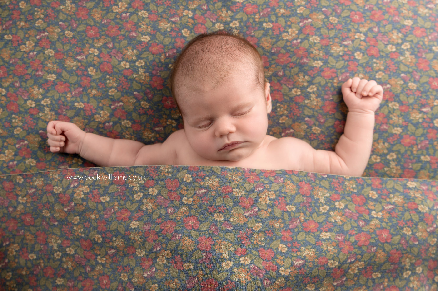 newborn baby girl laying asleep on a flowery blanket with her arms out stretched