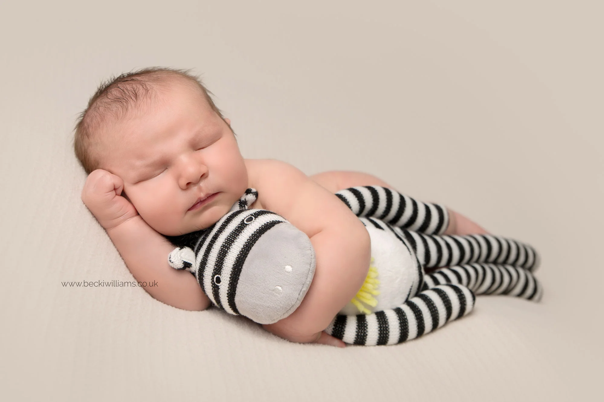 newborn boy laying asleep on his side hugging a sock monkey at his newborn photo shoot in hemel hempstead