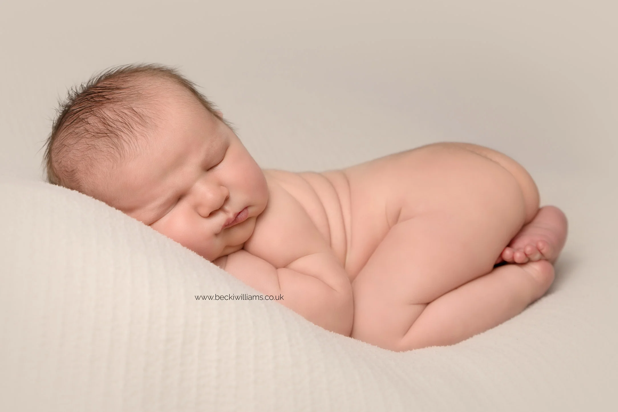 newborn boy laying asleep, curled up on his tummy for his newborn photo shoot in hemel hempstead