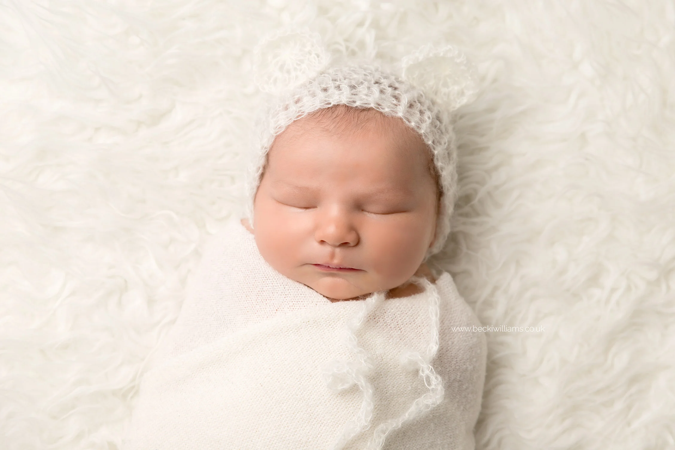 newborn baby boy, sleeping, wrapped in a white blanket, wearing a bear hat at his newborn photo shoot in hemel hempstead