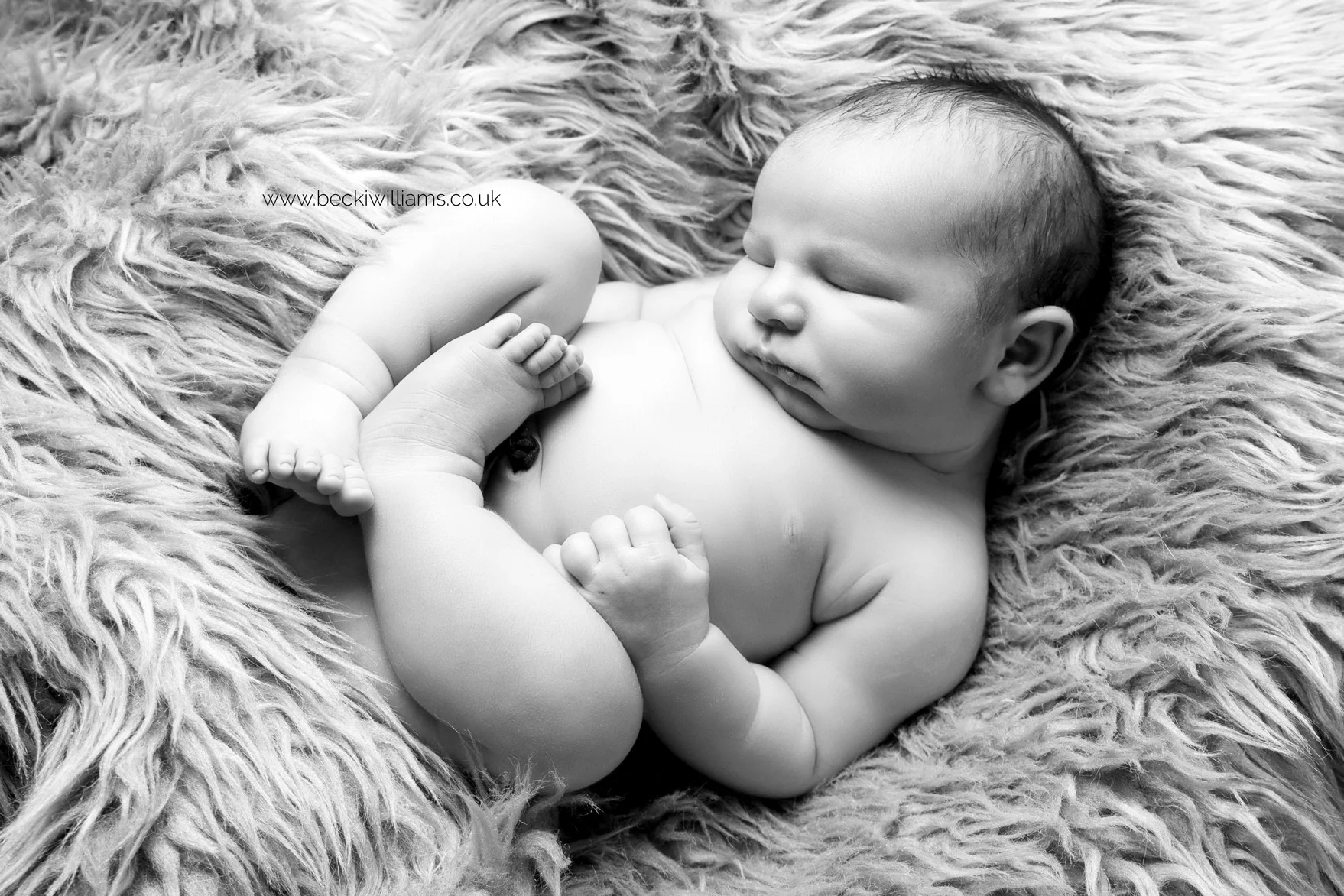 black and white image of a newborn baby boy laying asleep on his back on a fluffy blanket