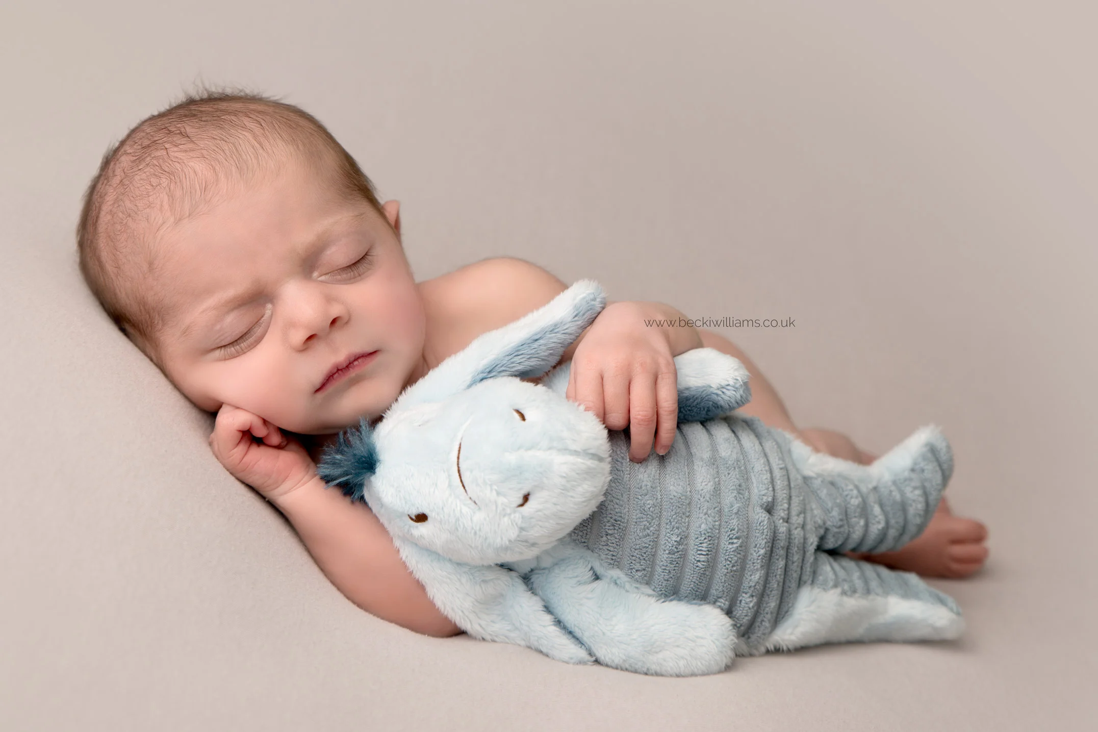 a baby girl asleep on her side cuddling a toy eeyore at her newborn photo shoot in hemel hempstead