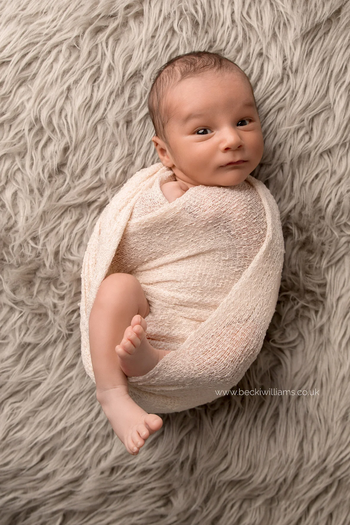 newborn baby boy wrapped in a cream wrap on a furry blanket for his newborn photo shoot in hemel hempstead