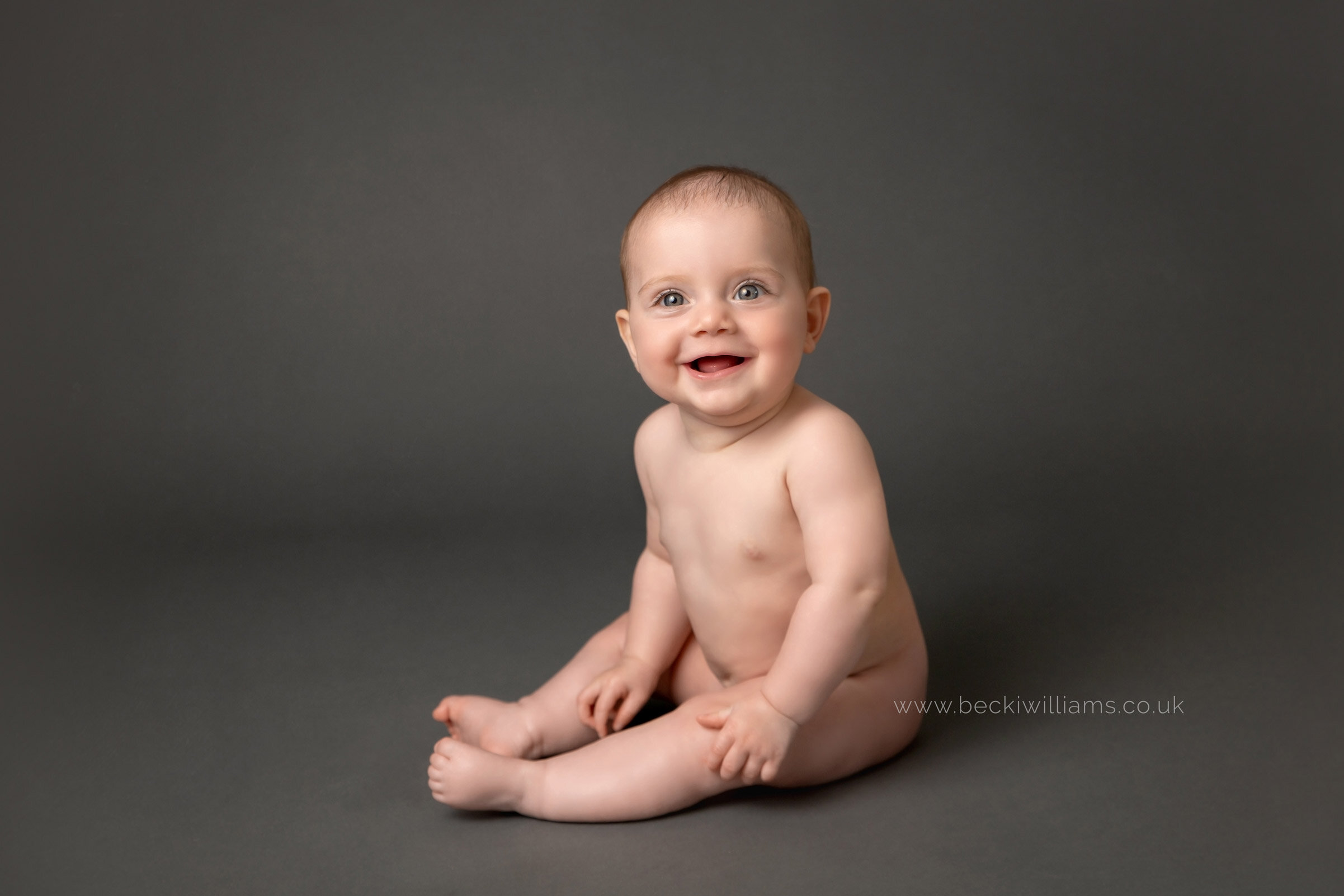 9 month old baby girl sitting on a dark grey backdrop at her professional baby photo shoot in Milton Keynes