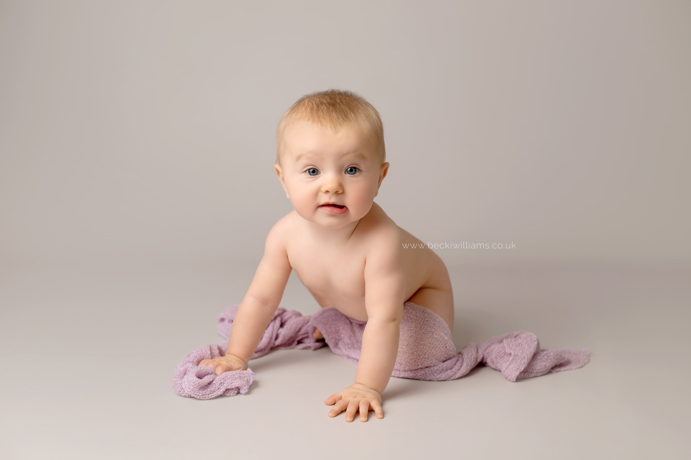 9 month old baby girl crawling towards the camera on a light grey backdrop