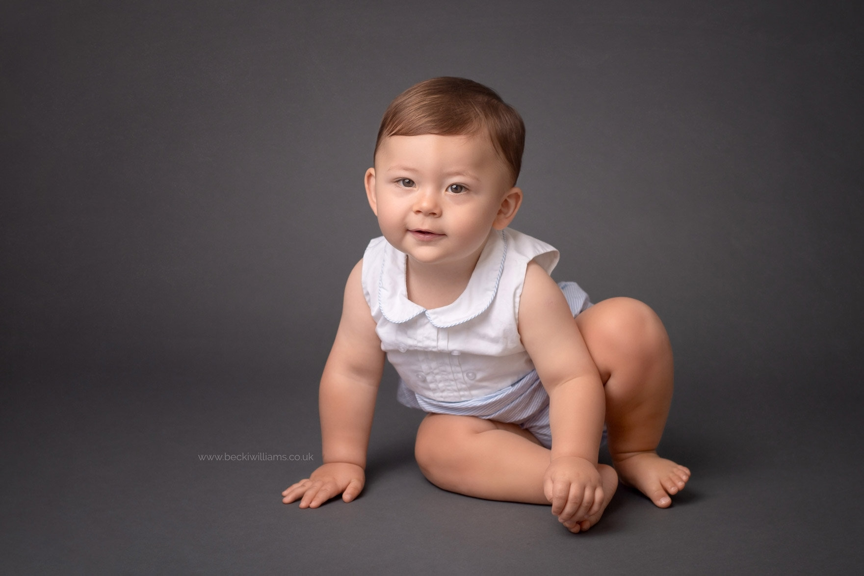 1 year old sits on the floor on a dark grey backdrop in Buckinghamshire