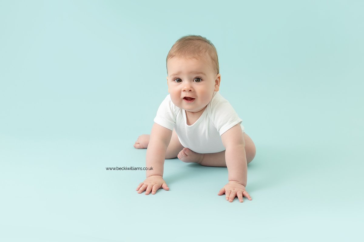 8 month old baby boy wearing a white vest on a baby blue backdrop