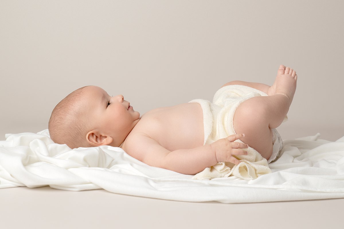 4 month old laying on a white blanket, which is on a light grey backdrop.  Taken by a photographer in Milton Keynes