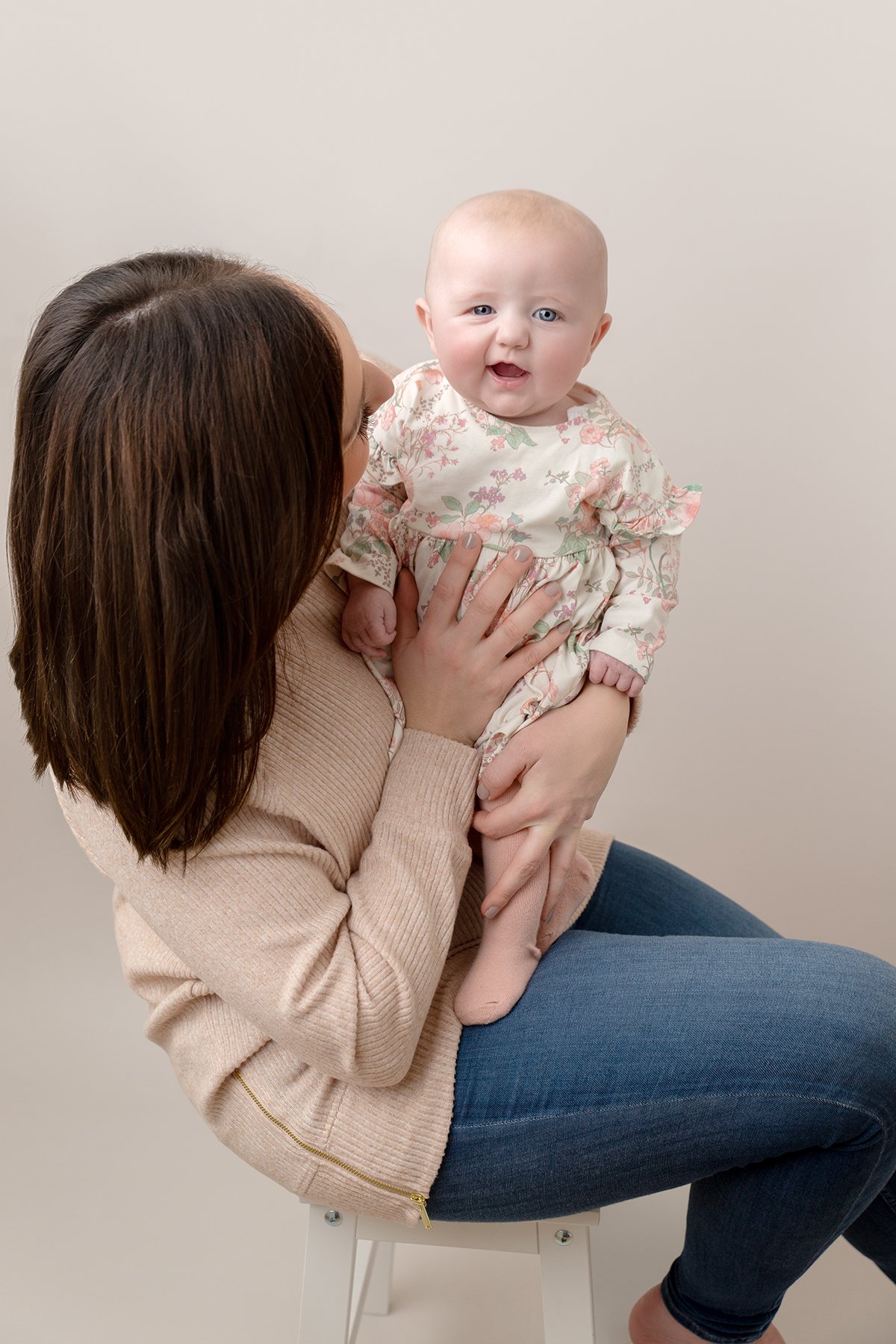 Mum sitting on a stool holding her 3 month old baby who is smiling at the camera