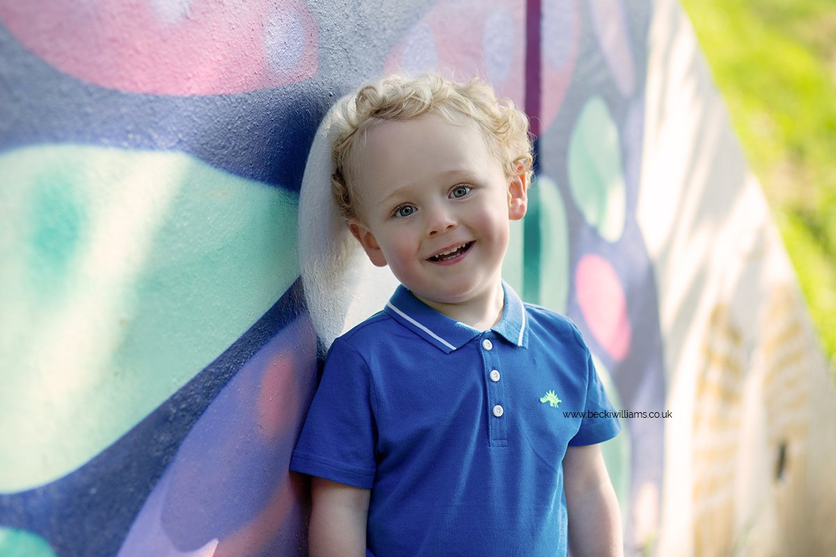 Young boy smiling at the camera in front of colourful wall