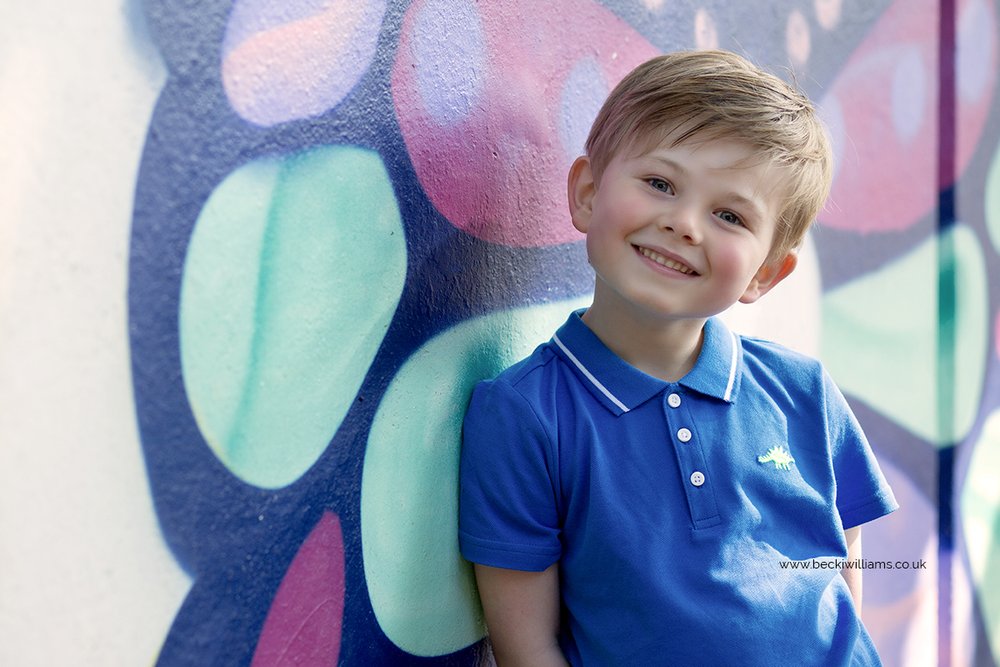 Young boy smiling at the camera in front of colourful wall