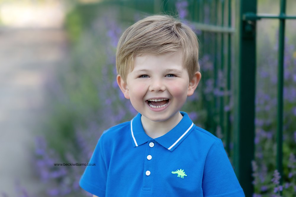 Young boy smiling at the camera in front of purple flowers