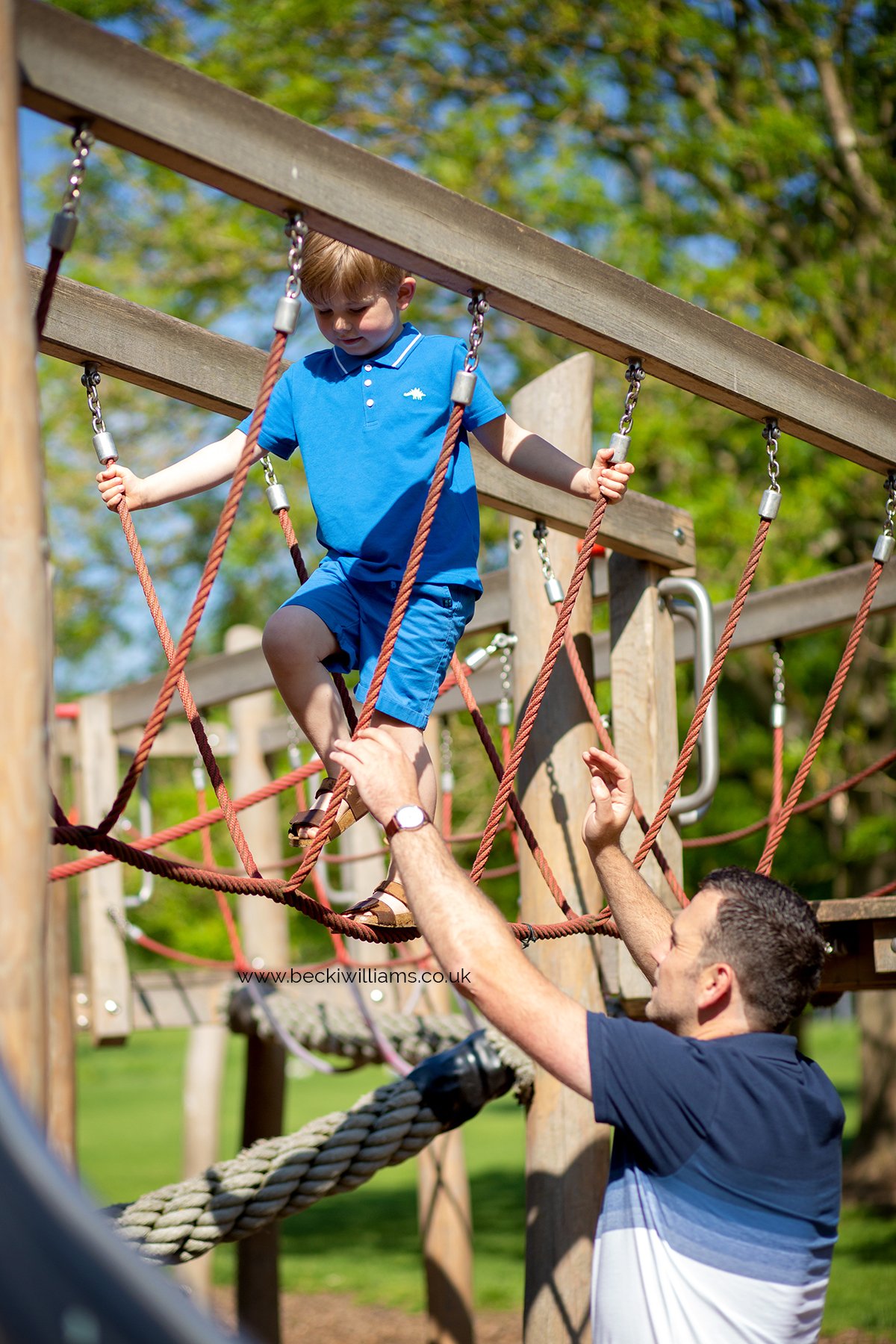 Young boy on a rope bridge.  Dad reaching up to help him