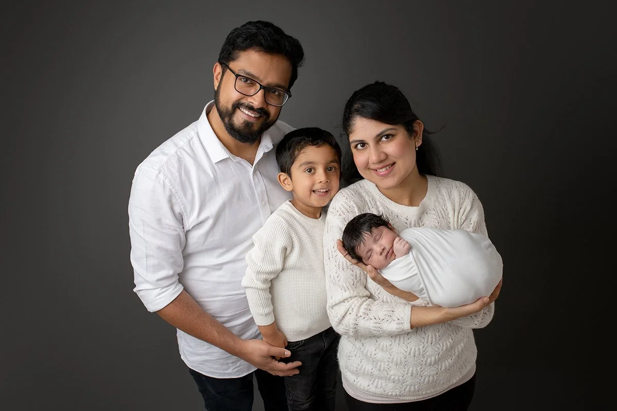 Mum, dad and brother holding a newborn baby at their newborn photo shoot