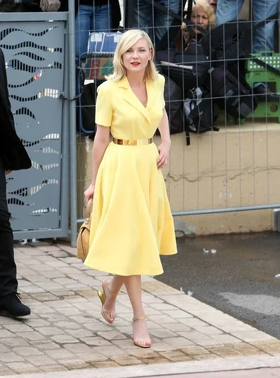 Kirsten Dunst channels Grace Kelly in a lemon-yellow Dior shirtdress and and a retro basket bag.