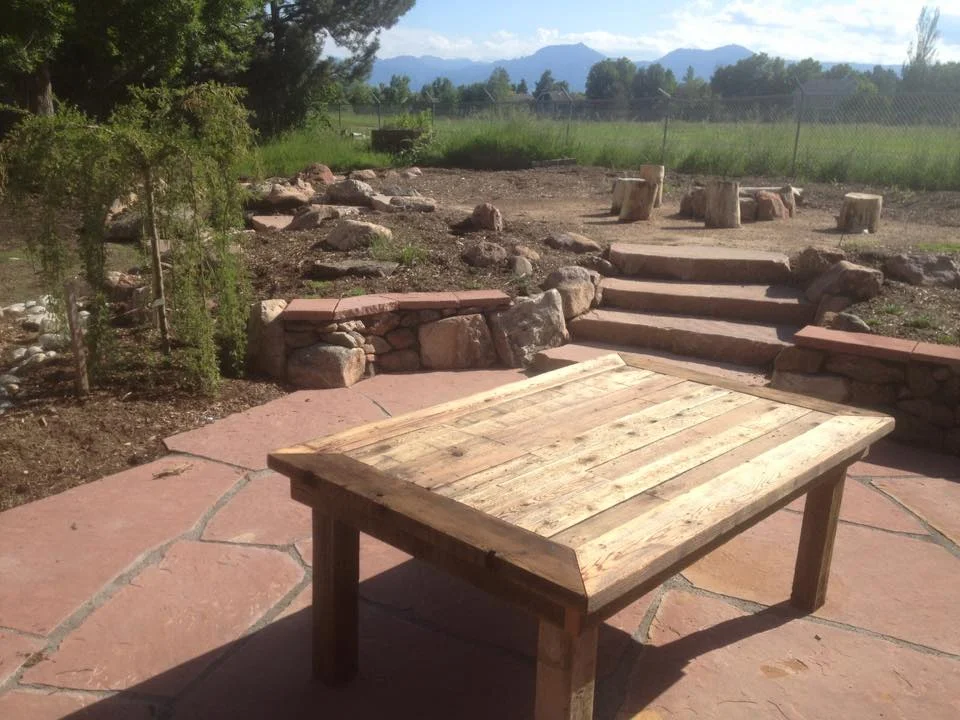 Boulder landscape design utilizes custom re purposed wood furniture to bring this living space to life.