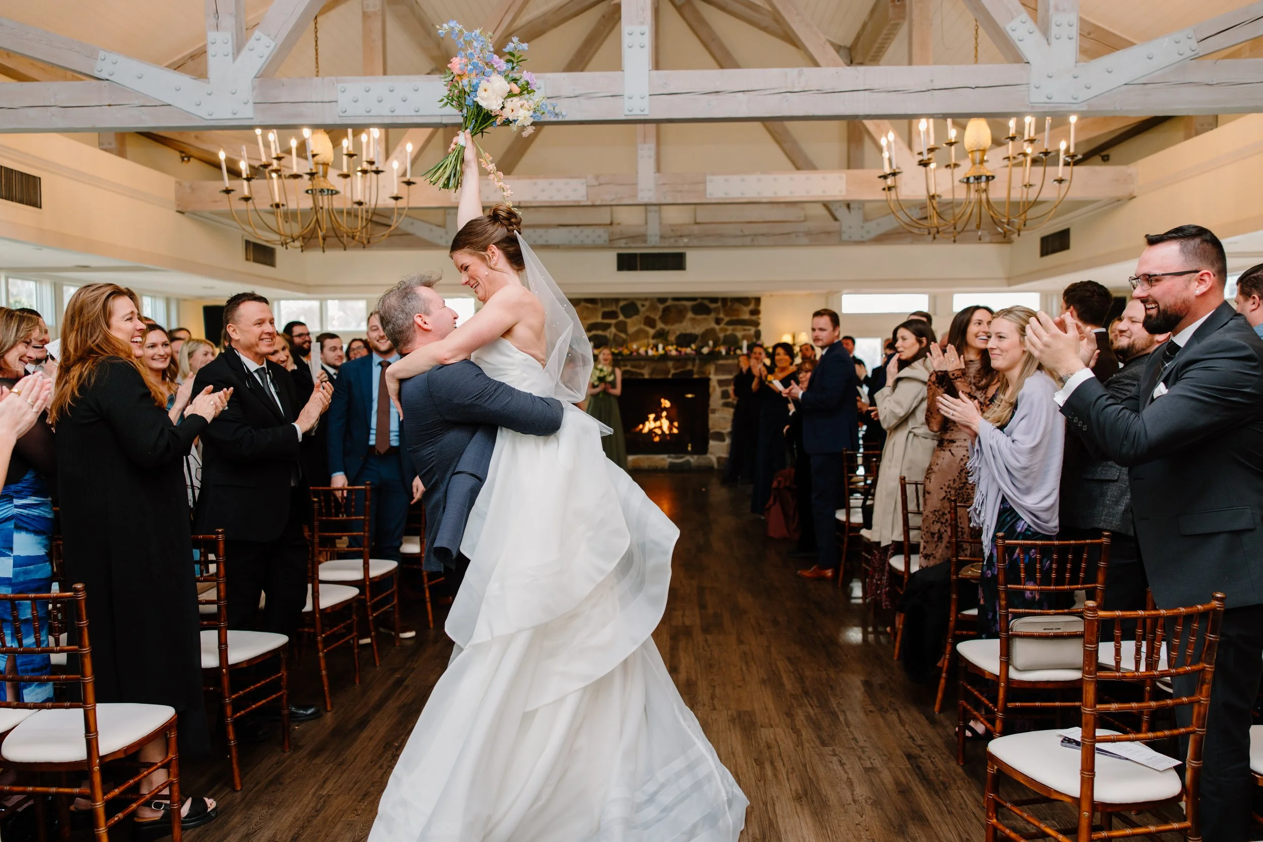 groom lifting bride up after first kiss, bride raising flowers over her head