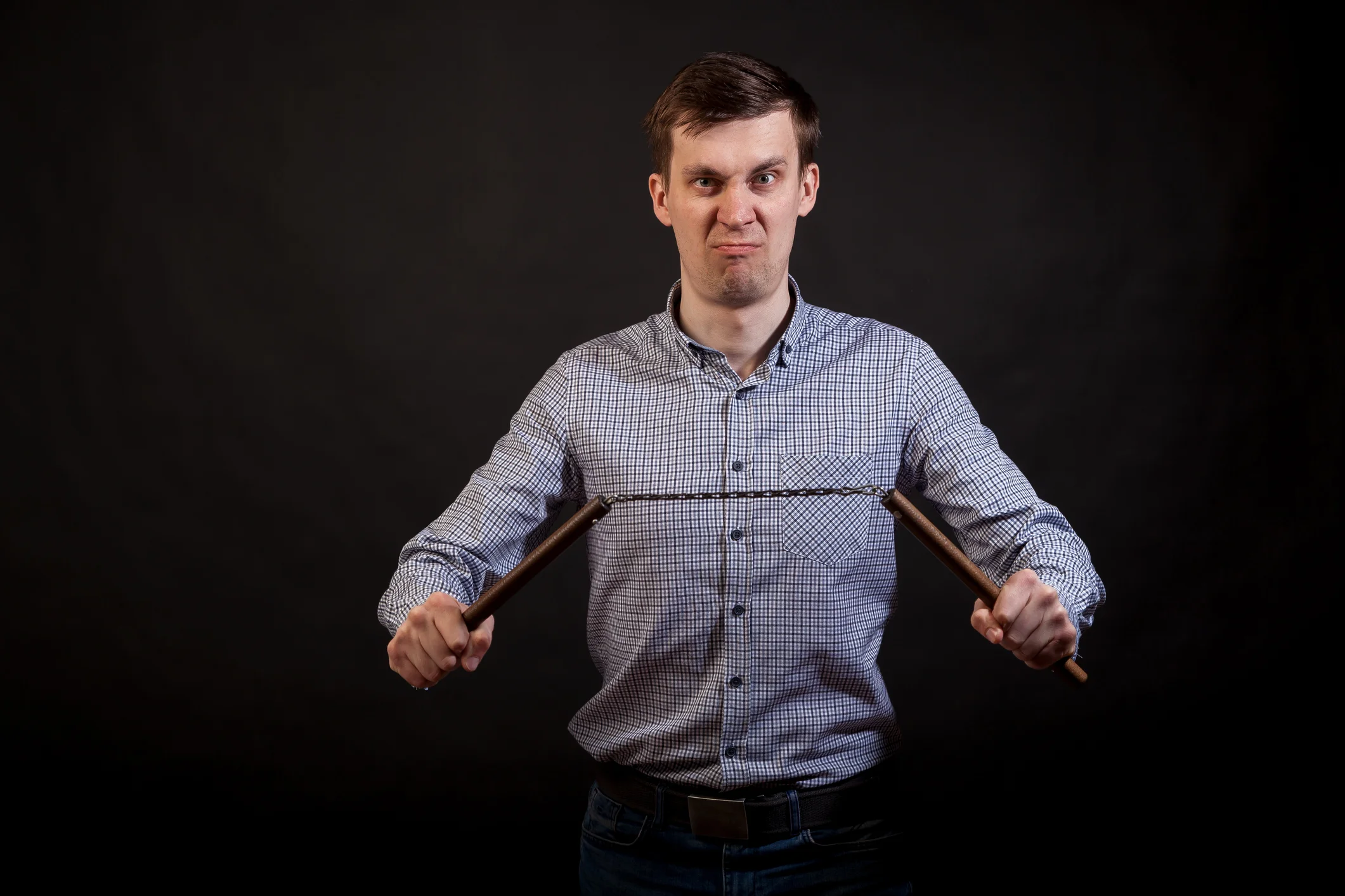 Dark-haired man in a plaid shirt "nholds a nunchuck in his hands "non black isolated background
