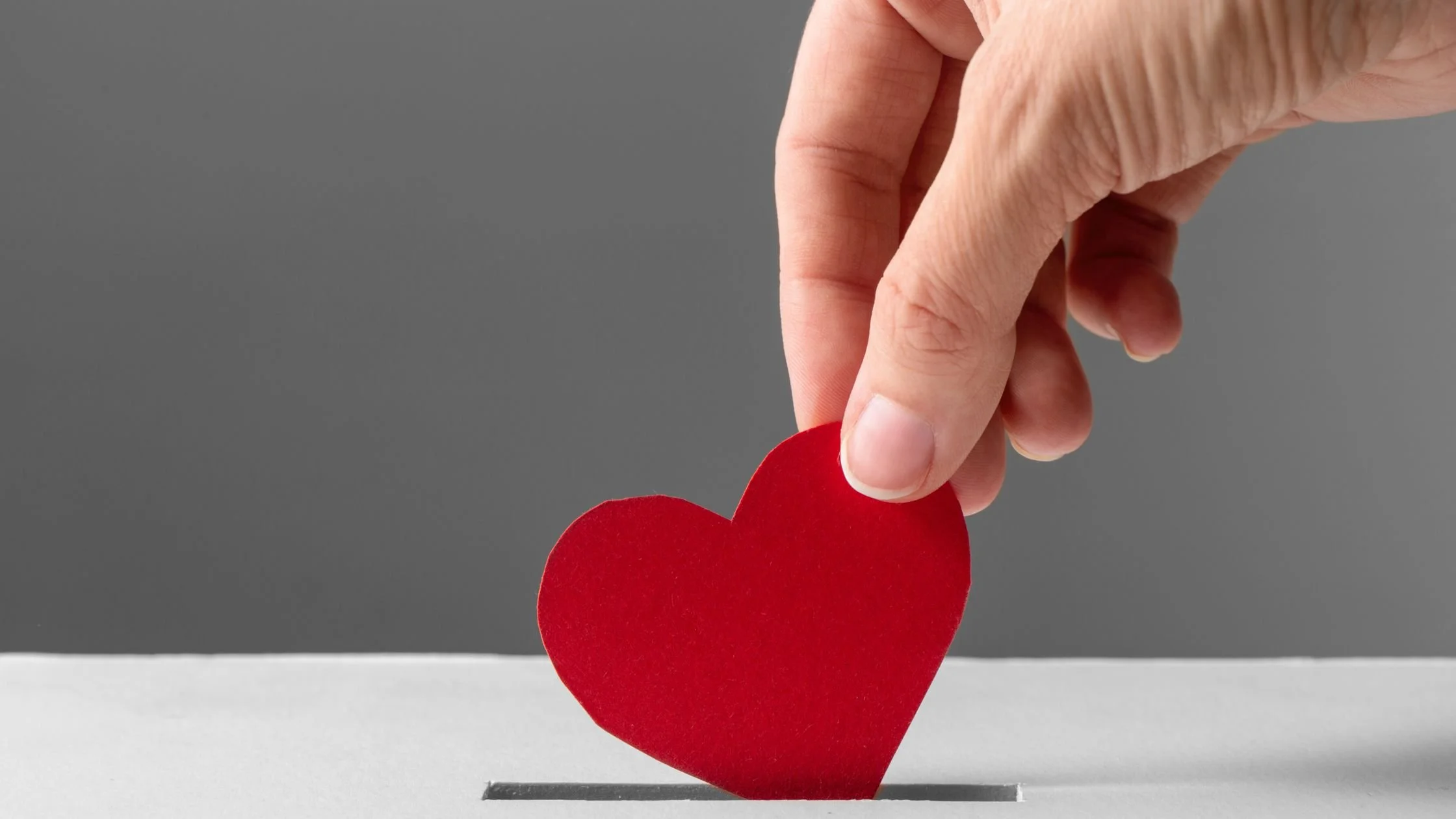 Hand holding a heart and placing it in a donation box