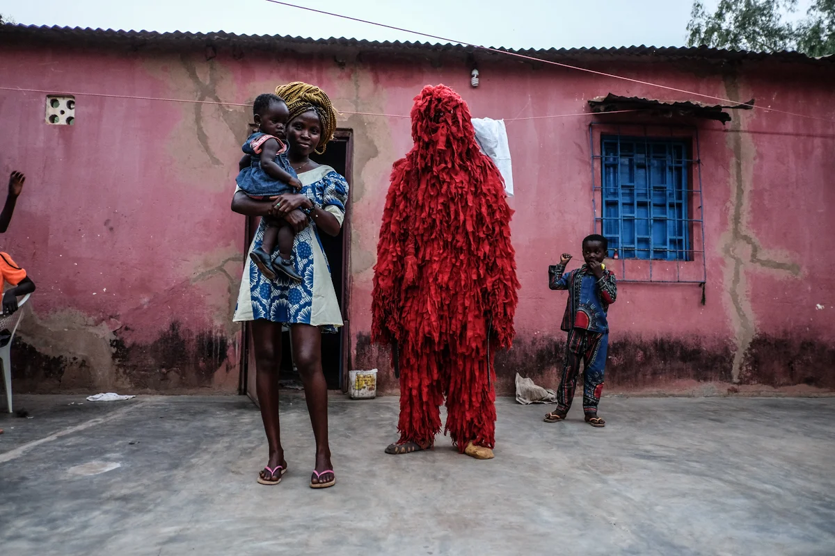Bissau, Guinea-Bissau (February 5, 2016) - A man dressed as Kankouran, the traditional Mandinga creature that chases away evil spirits after circumcision ceremonies in Mandinga tradition, stands with a woman dressed in modern clothing in a neighborhood in Bissau. The Kankouran was dressed up as part of Guinea Bissau's Carnaval celebrations each year. In Bissau each year teams from all over the country perform traditional dances, songs and more from a variety of Guinea Bissau's ethnic groups to compete in Carnaval. The celebrations blend traditional clothing and ceremonies with modern party elements such as dyed-blonde hair, bright pink wigs and plastic party hats.