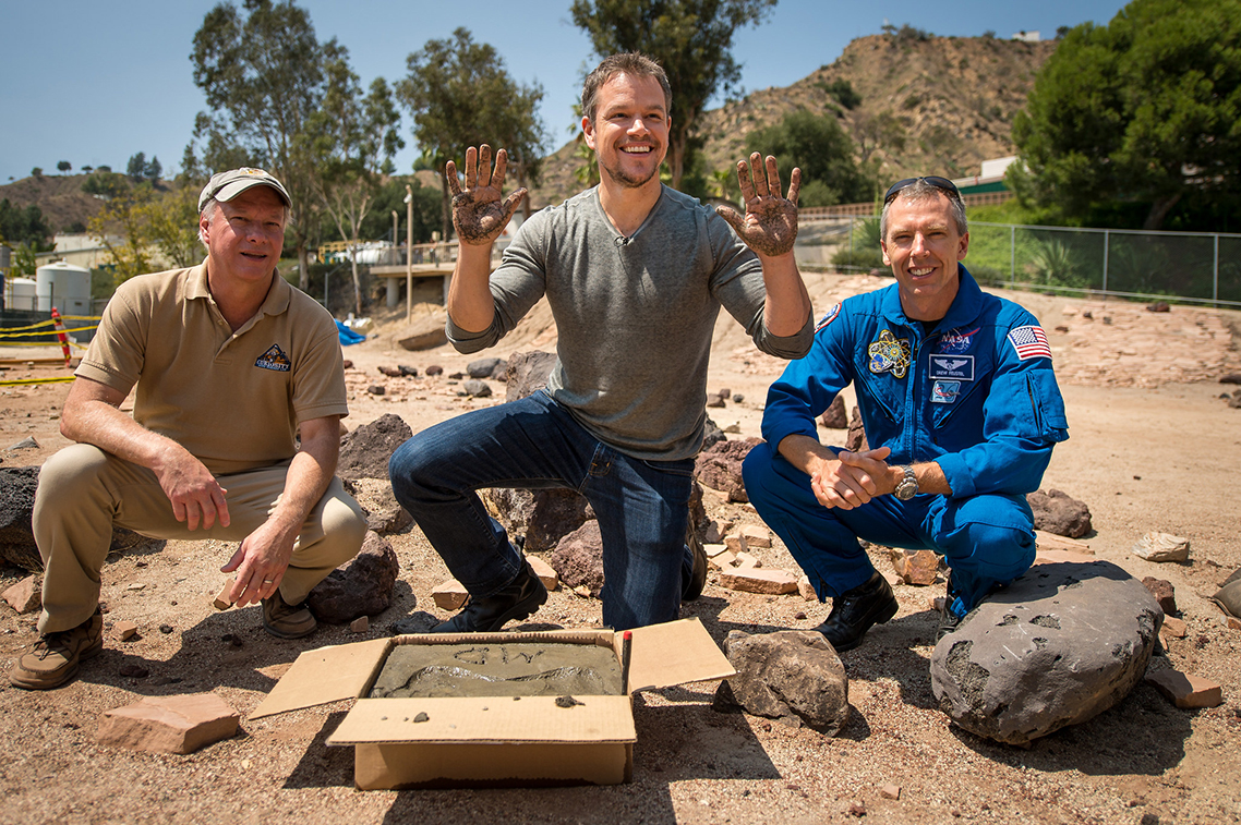 Actor Matt Damon, who stars as NASA Astronaut Mark Watney in "The Martian," smiles after making hand prints in cement at the Jet Propulsion Laboratory (JPL) Mars Yard while Mars Science Lab Project Manager Jim Erickson and NASA Astronoaut Drew Feustel look on. The movie is based on NASA data and realistically portrays what life would be like on Mars. (Bill Ingalls NASA/Flickr).