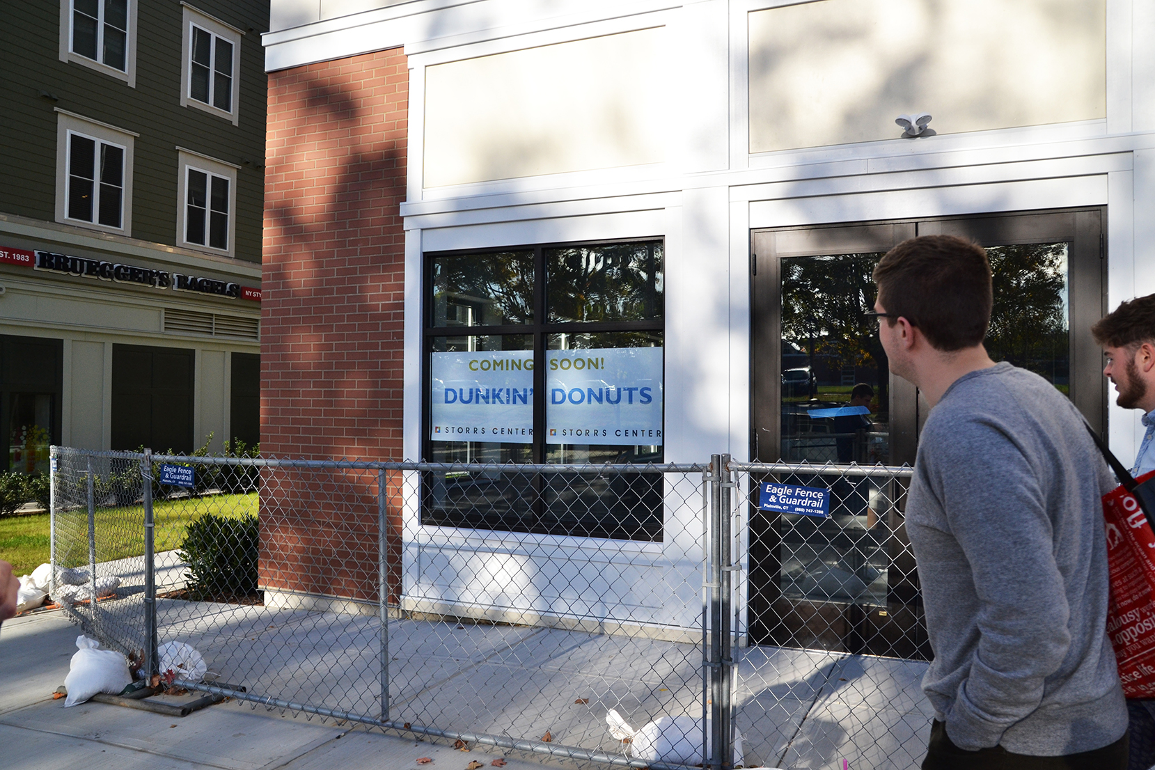 People walk past a coming soon sign on the future Dunkin' Donuts storefront in Storrs Center. Dunkin' Donuts will open a new location in Storrs Center by 2016 to “alleviate the pressure” on the Student Union location, said Dunkin Donuts’ franchisee, Derek Pacheco. (Amar Batra/The Daily Campus)