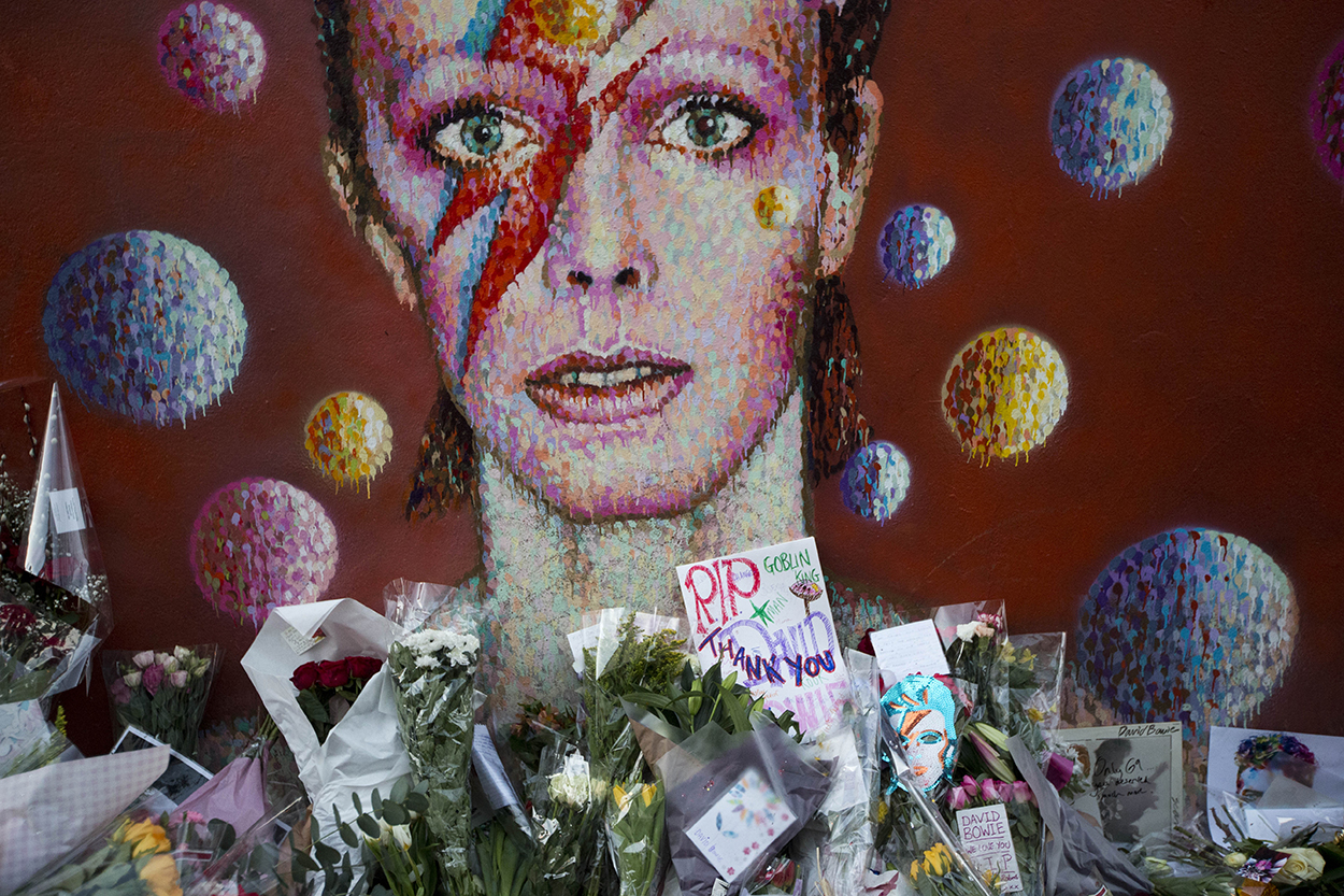Tributes lie beneath a mural of British singer David Bowie by artist Jimmy C in Brixton, south London, Tuesday, Jan. 12, 2016. Bowie , the other-worldly musician who broke pop and rock boundaries with his creative musicianship, nonconformity, striking visuals and a genre-spanning persona he christened Ziggy Stardust, died of cancer Sunday aged 69. He was born in Brixton. (AP Photo/Matt Dunham)