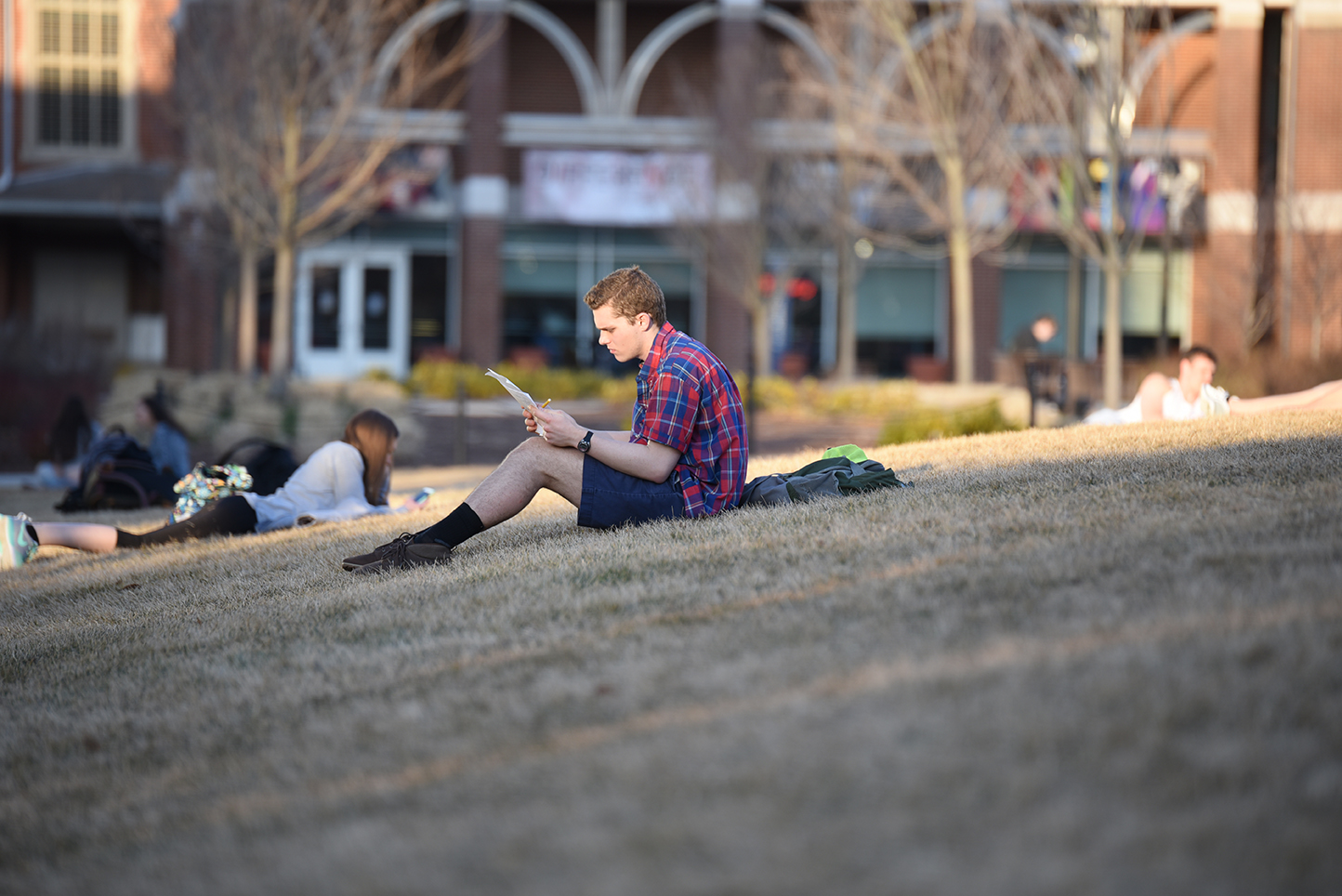 A student is reading his paper at the turf ground behind the Student Union. (Zhelun Lang/The Daily Campus)